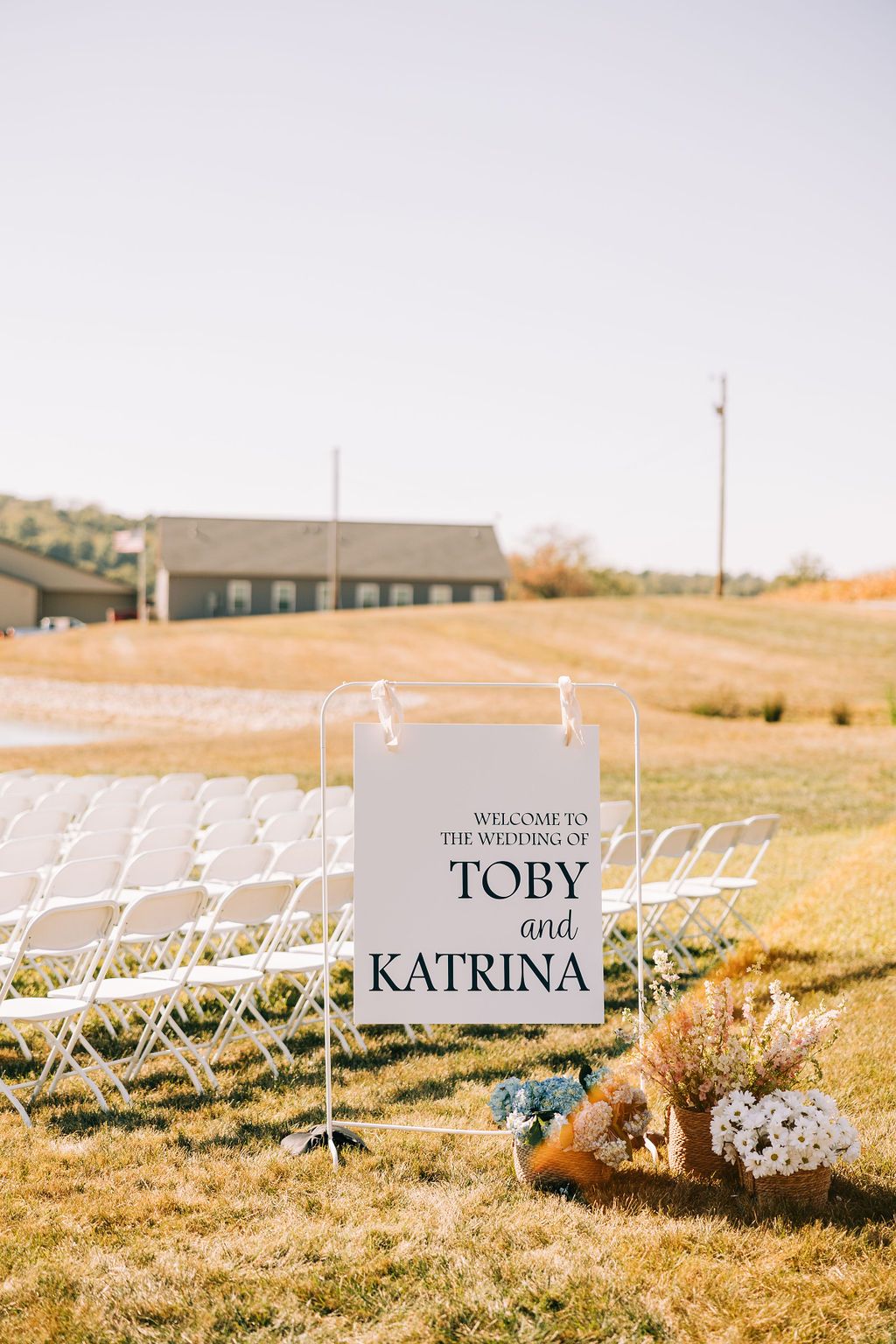 White name cards displayed on stakes in a grassy field during a rustic outdoor event setup.