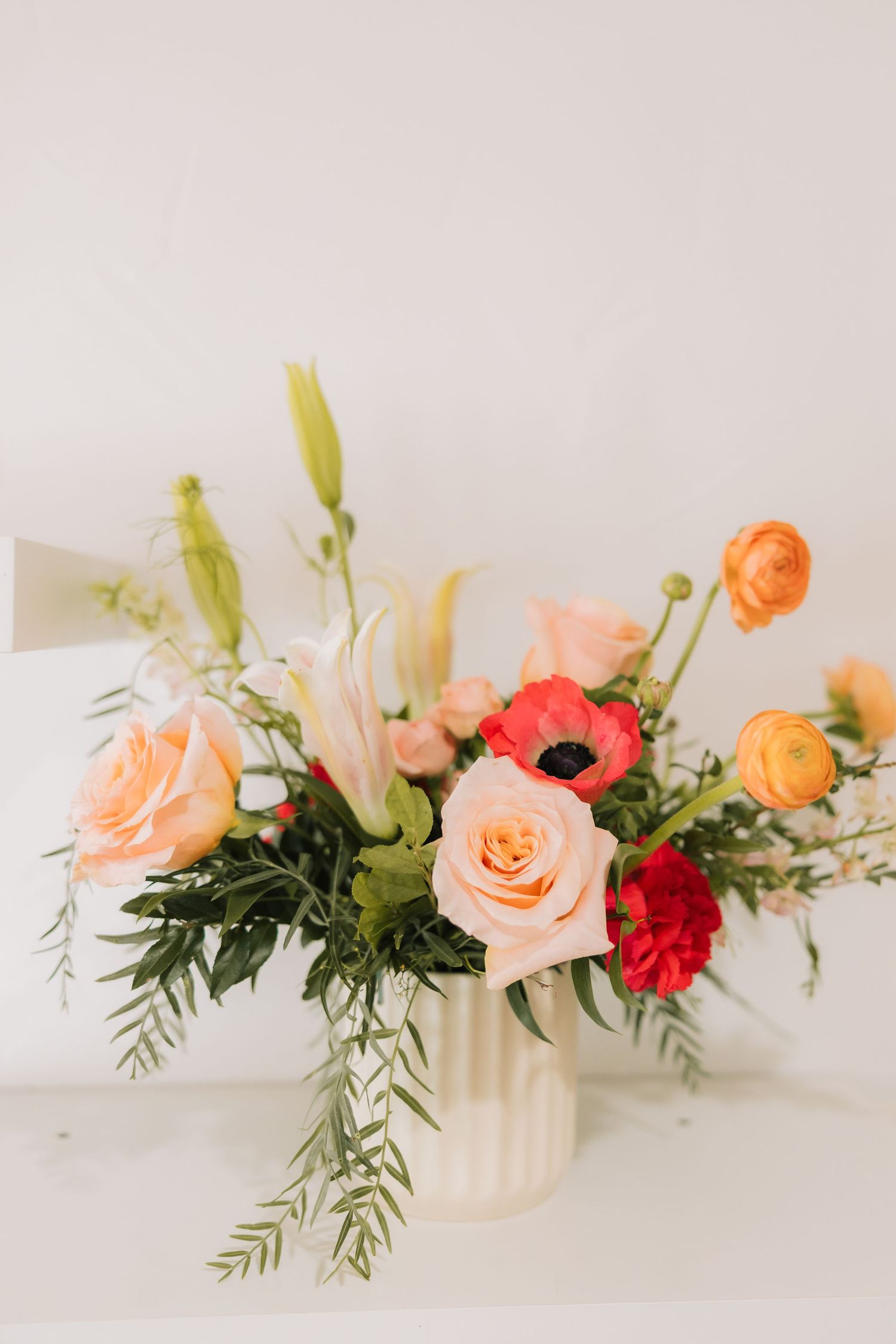 A delicate floral arrangement featuring peach and red roses with greenery on a white surface.