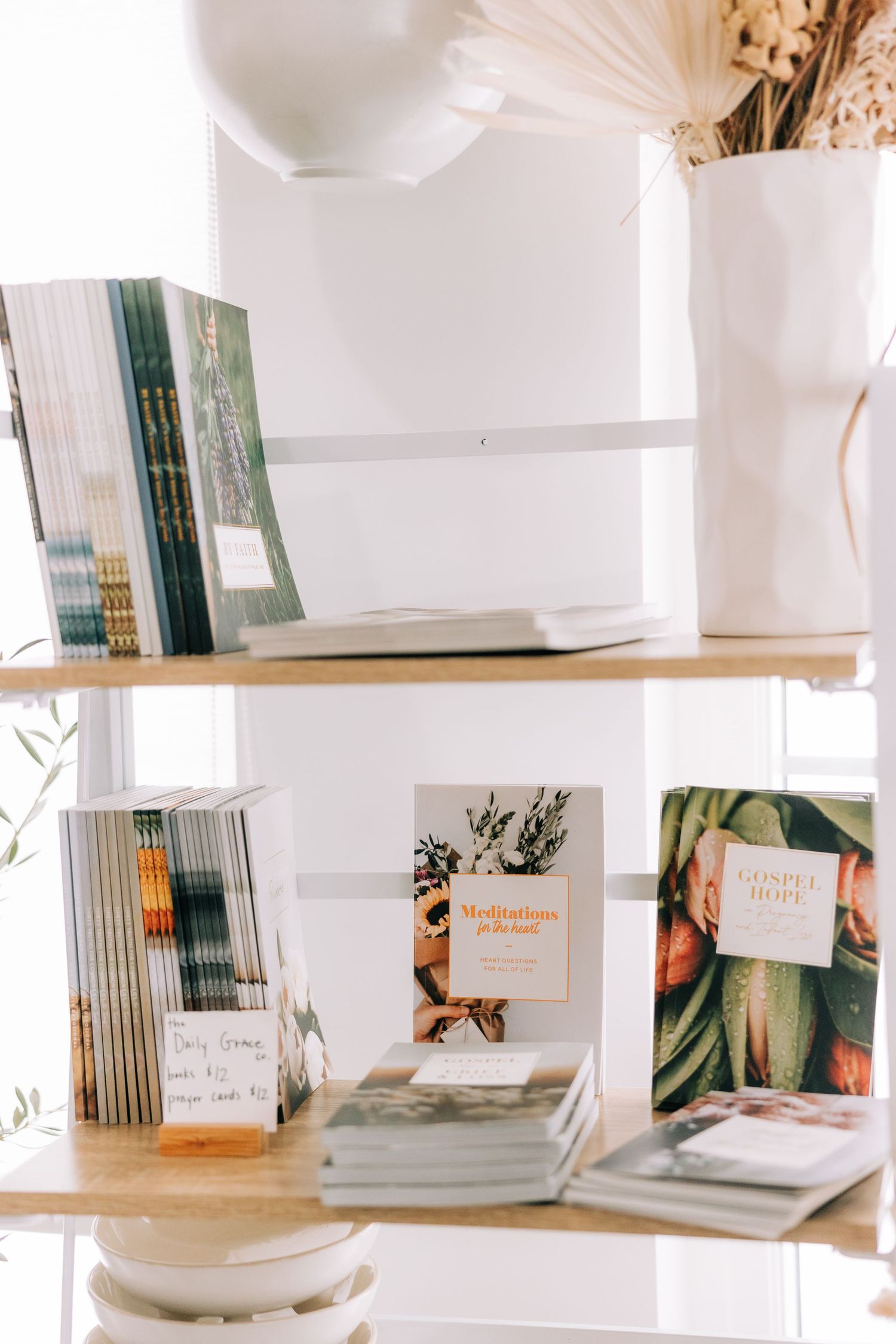 Aesthetic shelf display of books and magazines with white ceramic vases in natural light.