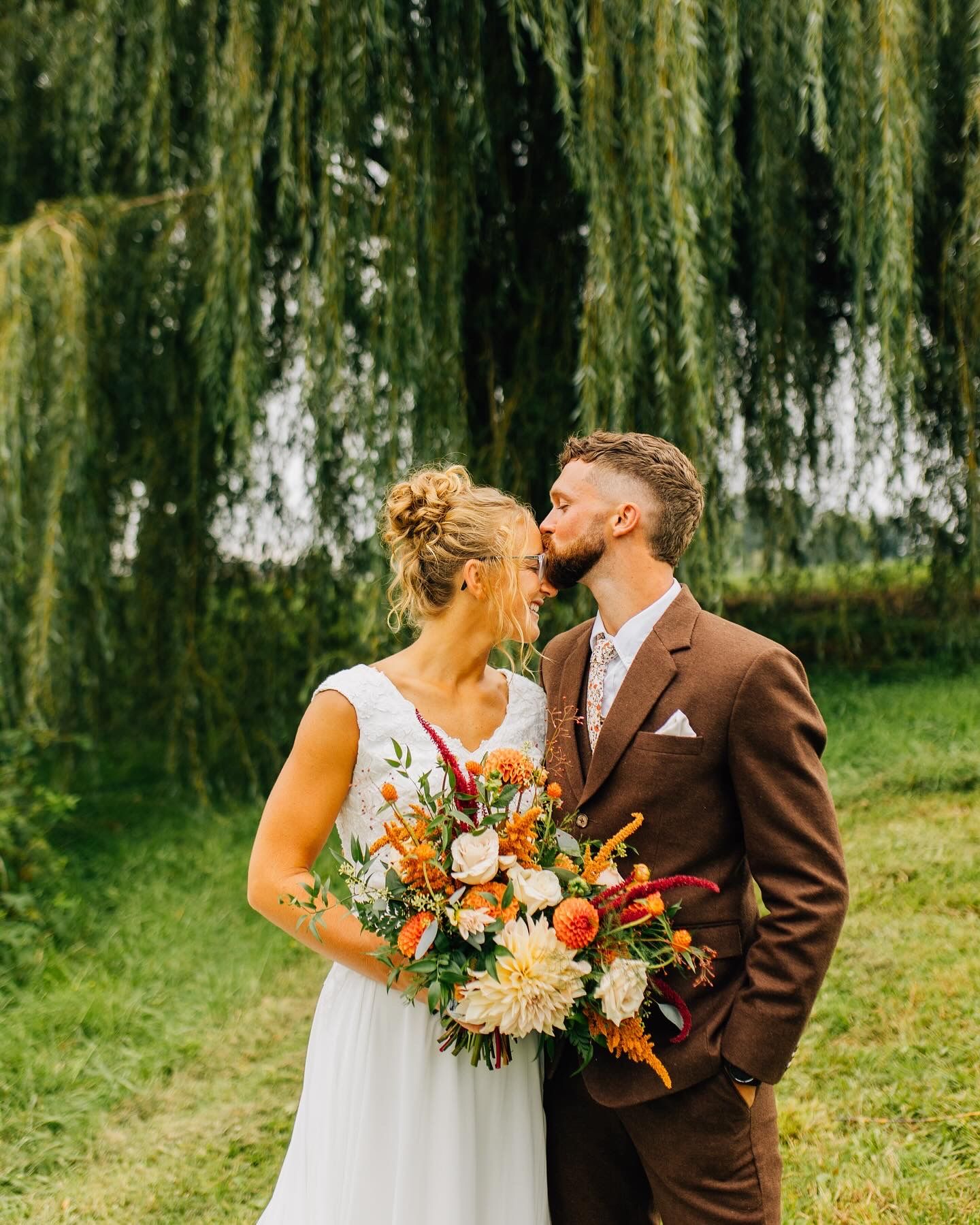 Wedding couple shares romantic moment against backdrop of flowing willow trees.