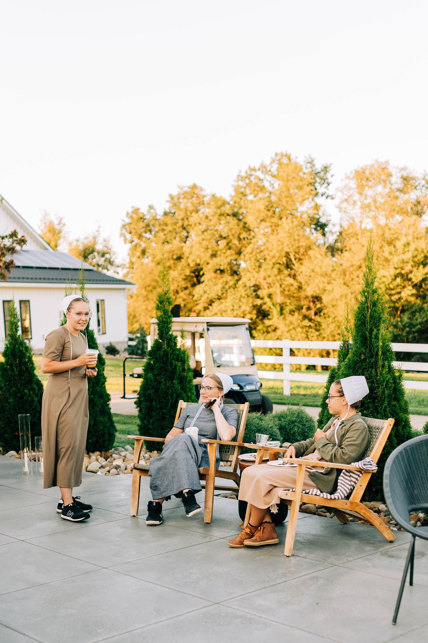 People relaxing on chairs on a patio with golden autumn trees in the background.