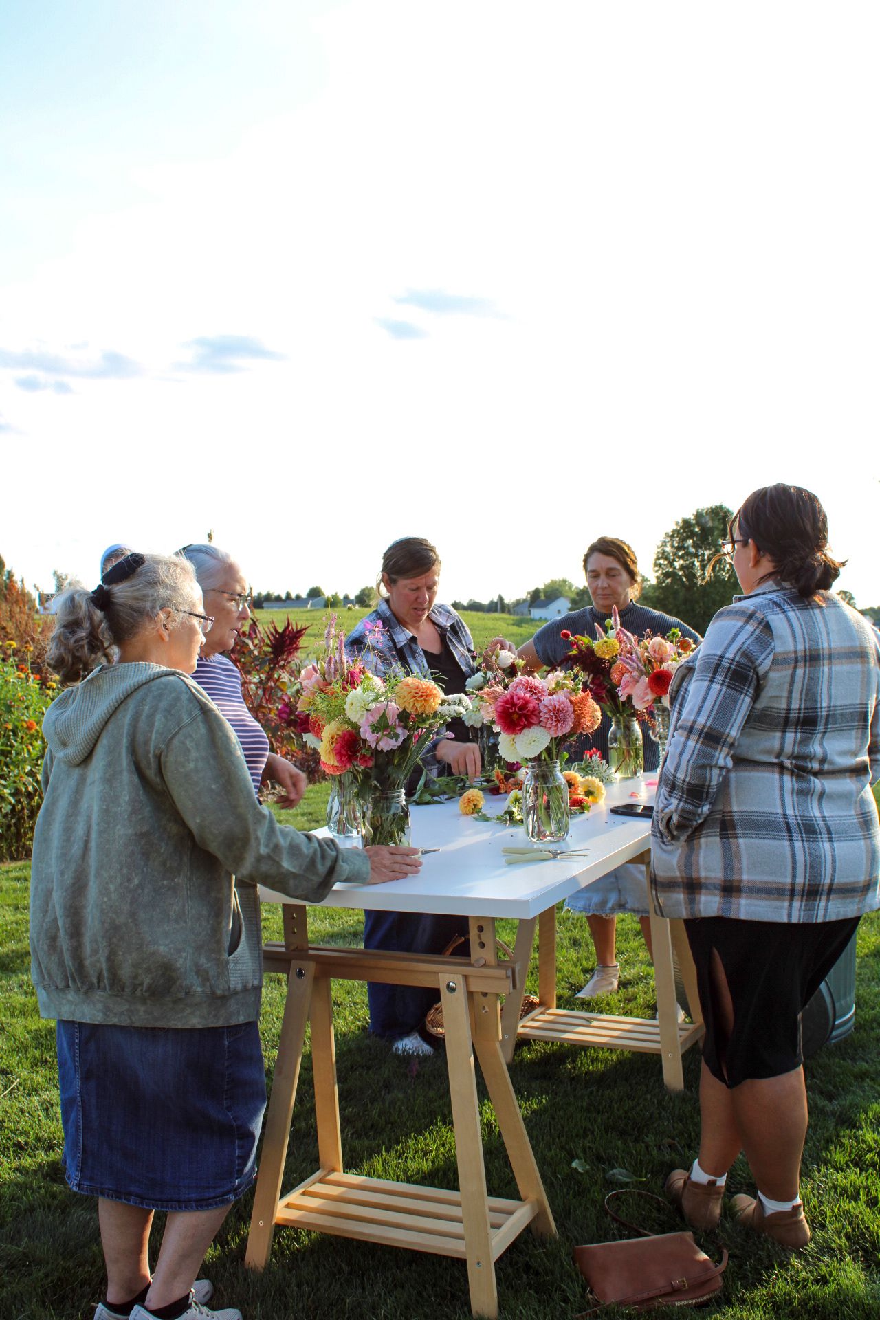 People gathered around a table arranging colorful flowers at an outdoor workshop in a garden setting.