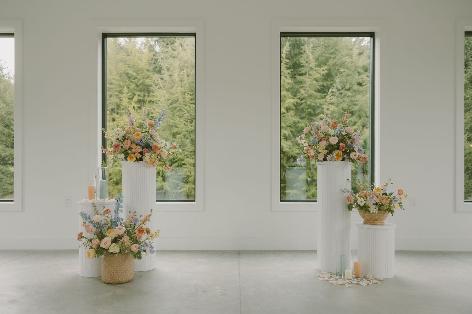 Minimalist white venue space decorated with elegant floral arrangements framing forest views through windows.