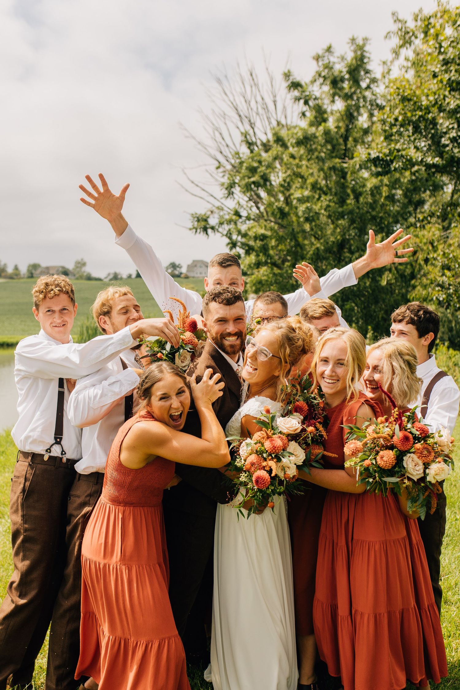 Energetic group photo of wedding party celebrating outdoors with fun poses.