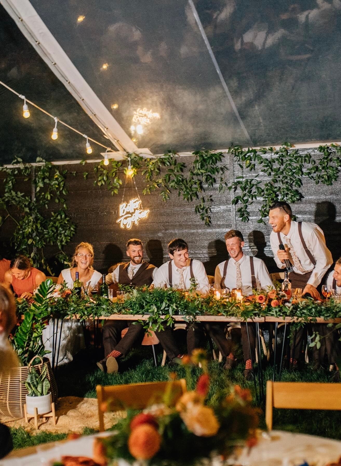 Wedding reception table decorated with greenery garland and string lights in evening setting.