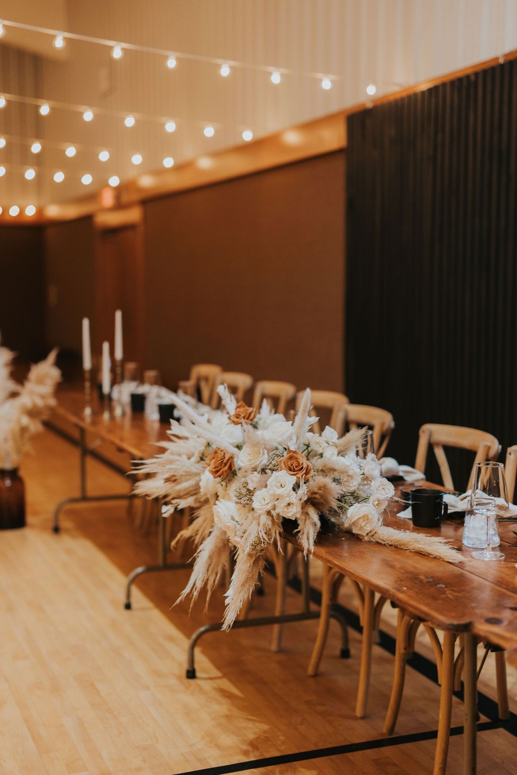 Rustic wooden dining table decorated with pampas grass and candles for an elegant wedding reception setup.