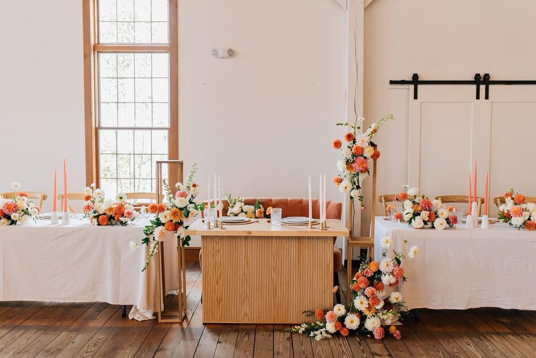 Long reception tables decorated with coral florals and taper candles in a bright white venue.
