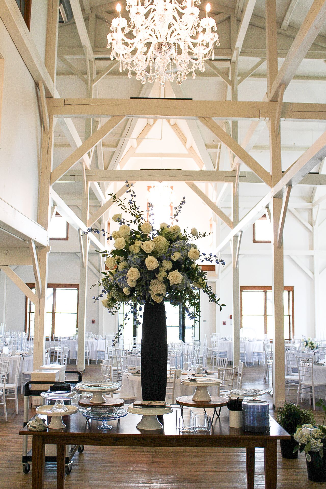 Grand wedding venue with crystal chandelier and tall floral centerpiece in white and cream tones.