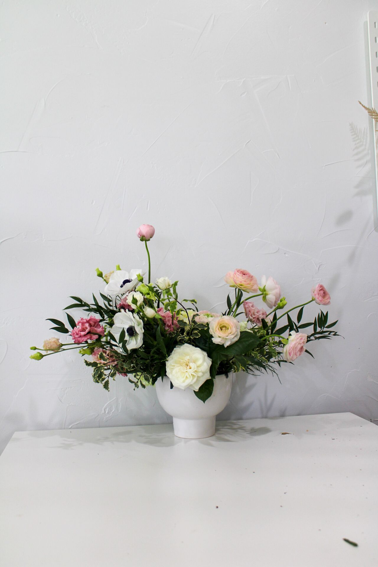 Romantic arrangement of pink and white garden roses with mixed greenery in white vase.
