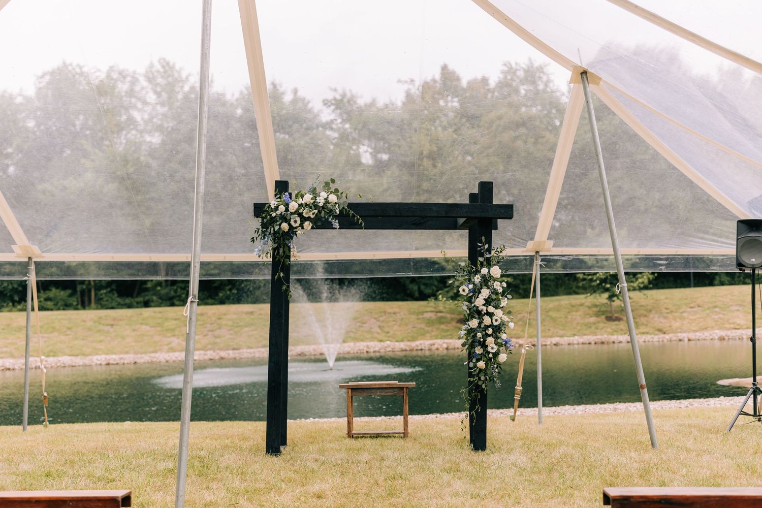 A wooden archway decorated with white flowers and greenery under a wedding tent.