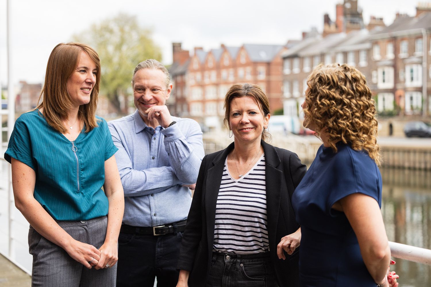 Four professionals networking outdoors near a waterfront, engaged in friendly conversation on a bright day.