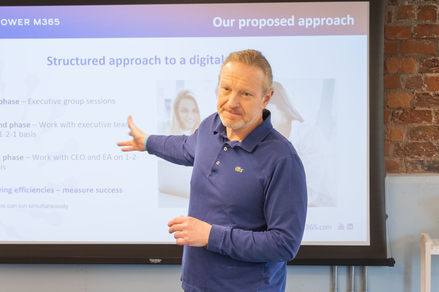 A man presents a digital strategy slide on a projector screen in a modern office meeting room.