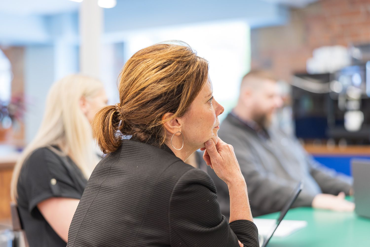 Professional woman in black jacket sits thoughtfully at a conference table during a business meeting.