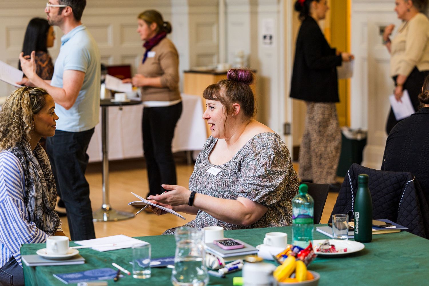 Women engaged in lively discussion at a conference table during a professional networking event in an elegant hall.