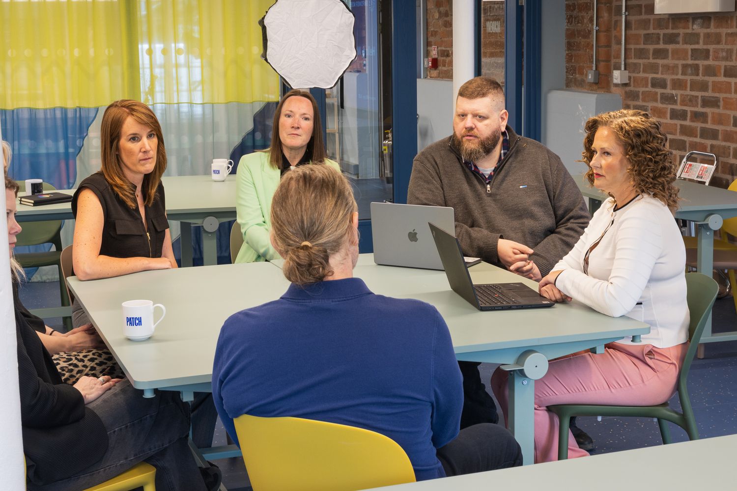 Group of professionals having a meeting around a table with a laptop in a colorful office environment.