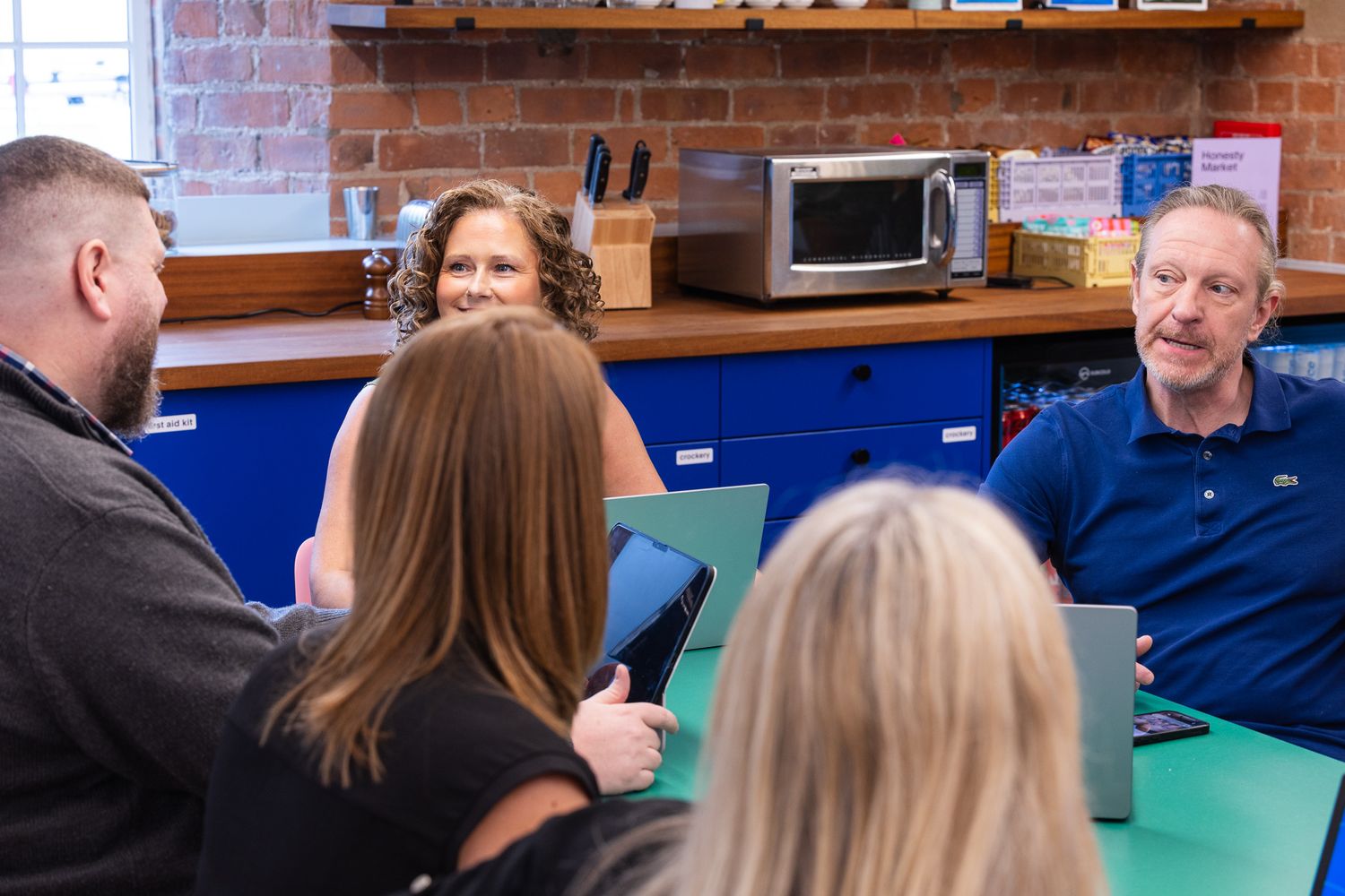 Group of colleagues having a casual business meeting in a modern office kitchen with blue cabinets.