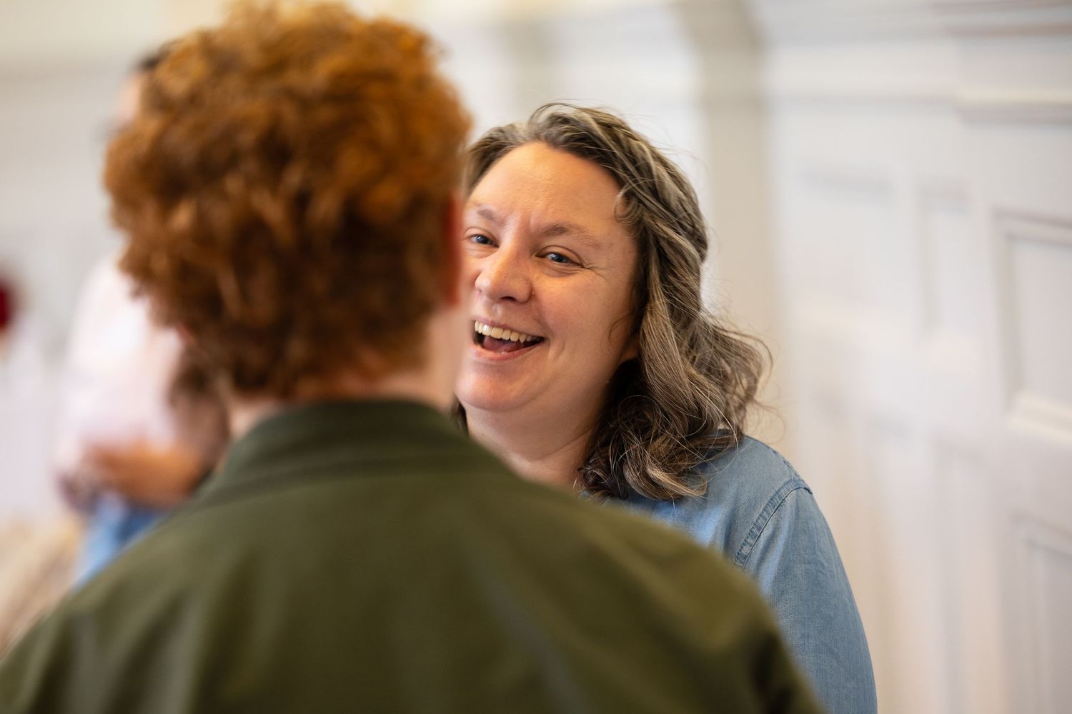 Two women sharing a joyful conversation, one laughing warmly in a bright indoor setting.