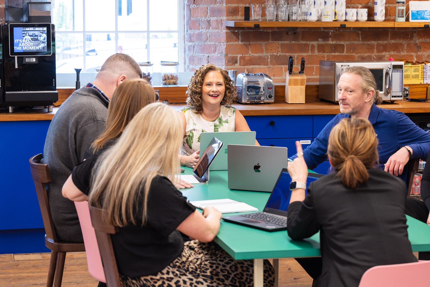 Group of professionals having a collaborative meeting around a green table in a modern brick-walled cafe workspace.