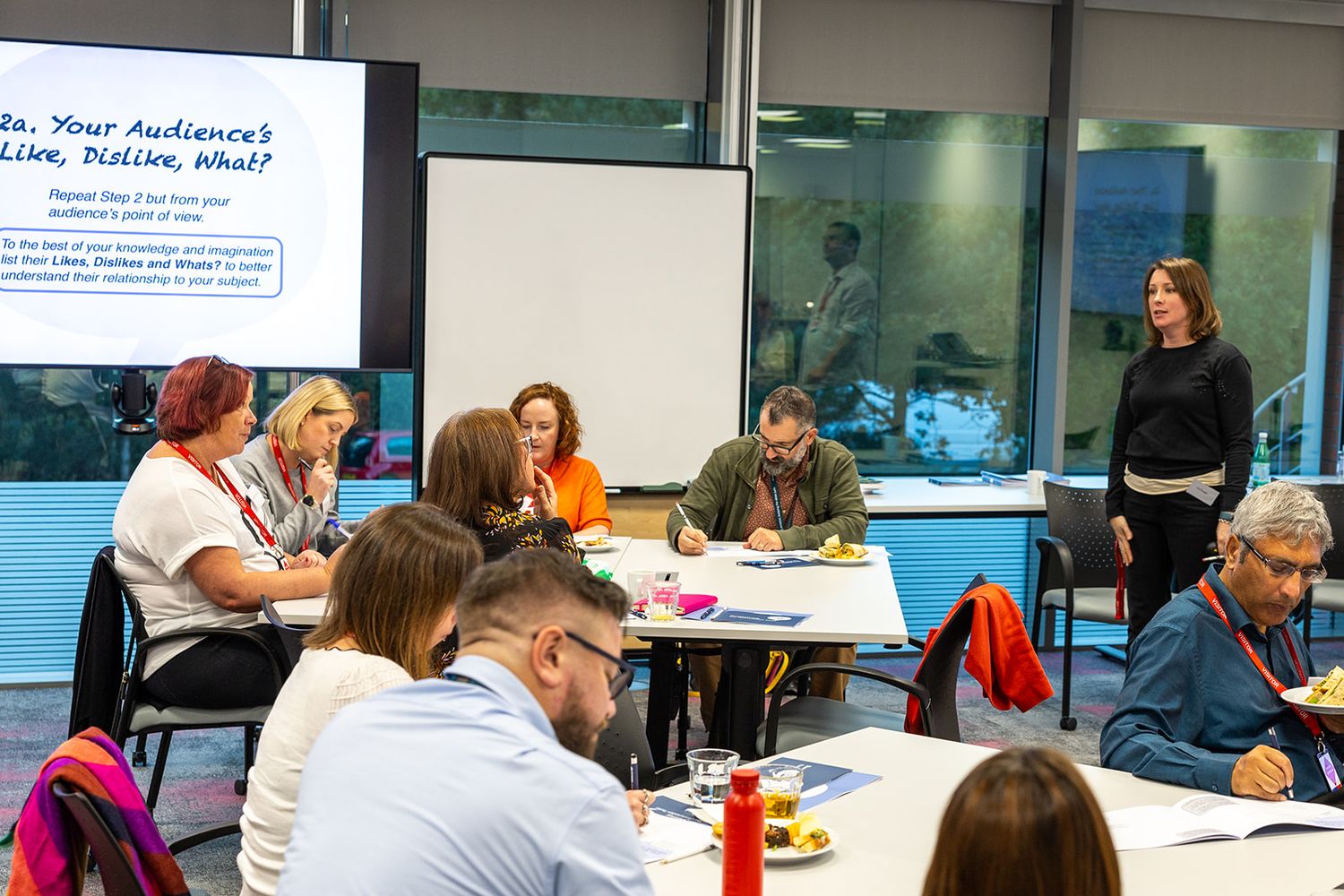 Professionals attend a business workshop seminar with presenter standing near projector screen in modern conference room.