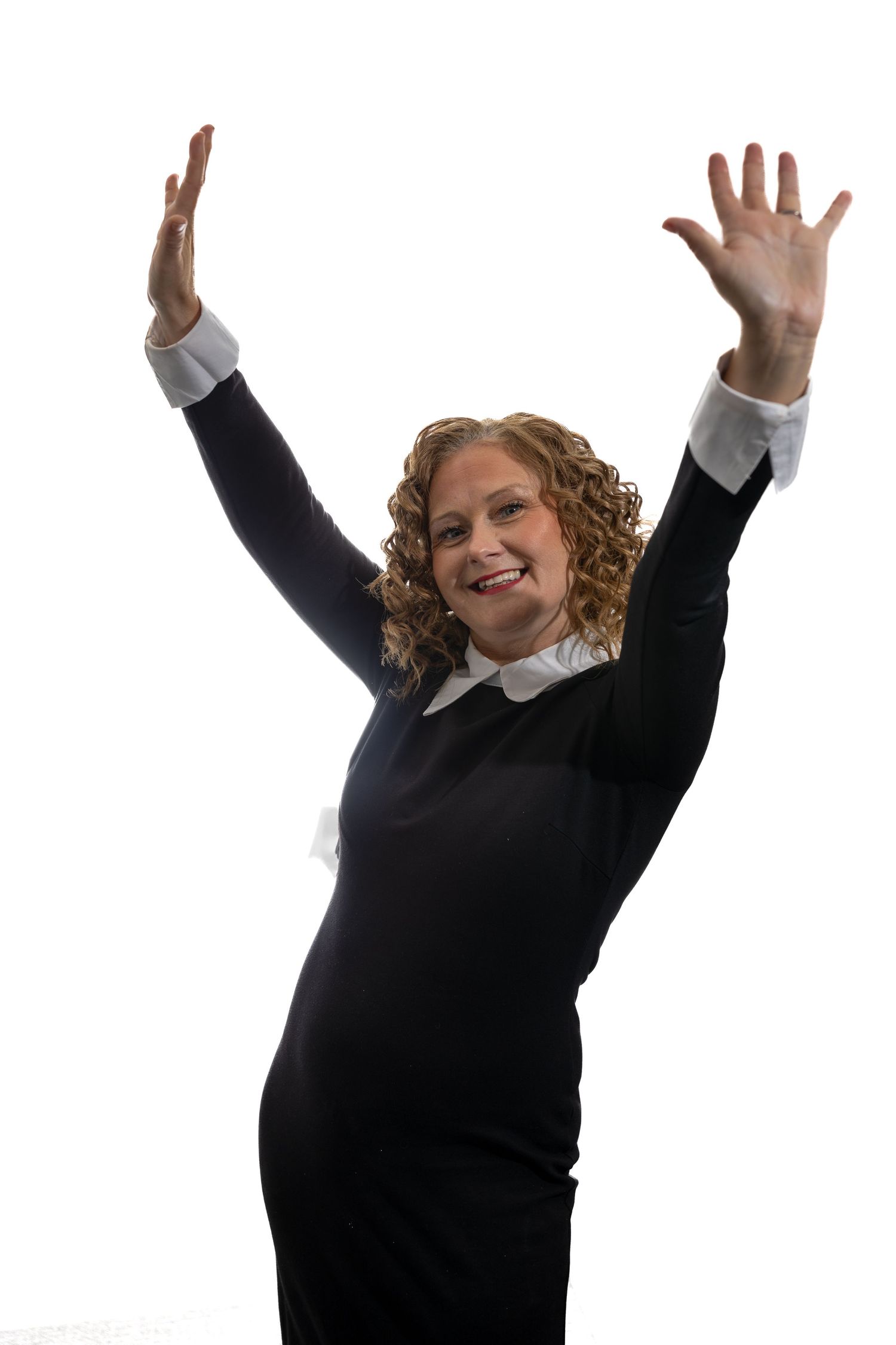 Happy businesswoman in black dress celebrating with raised hands on white background.