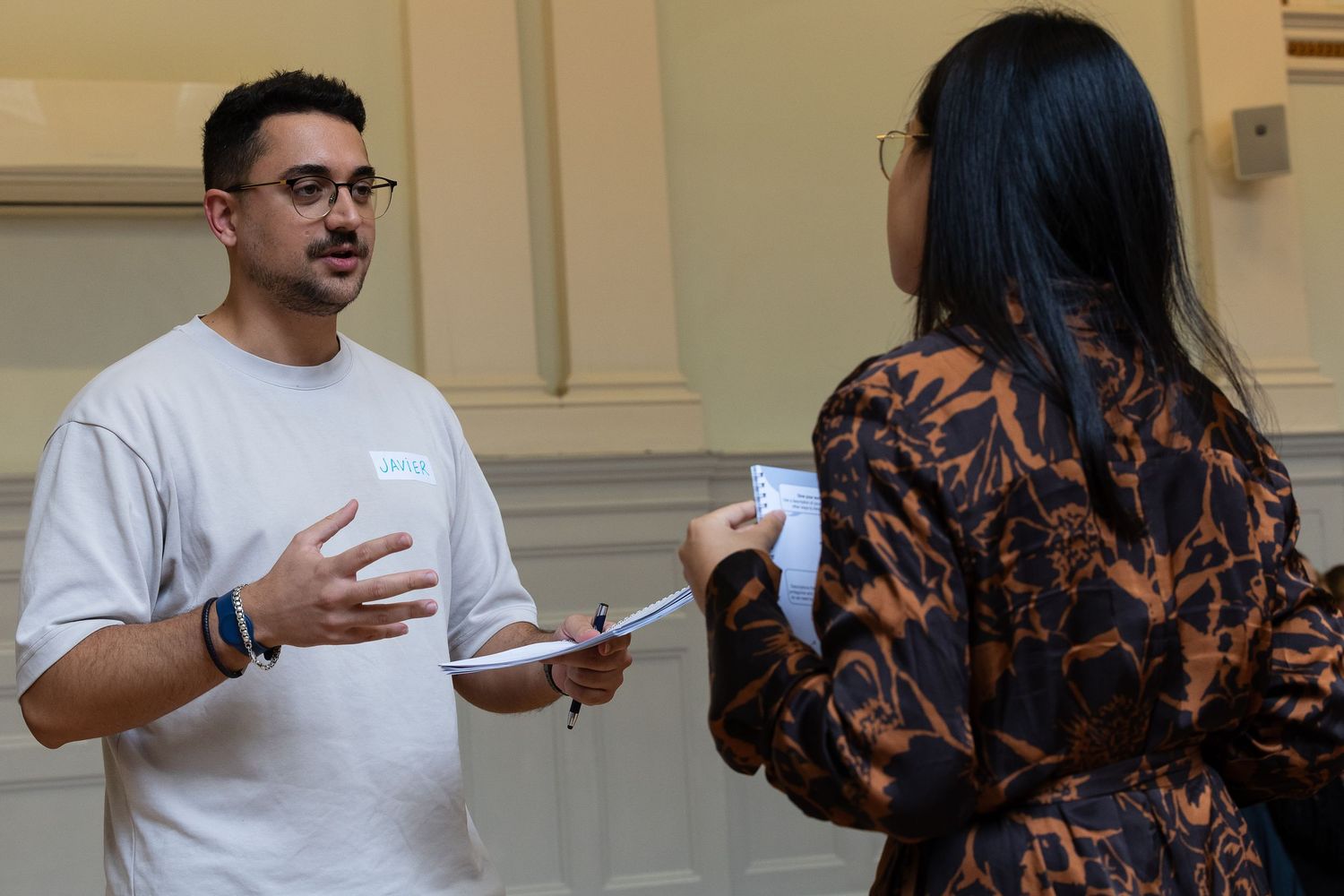 Two people engaged in conversation, man in white t-shirt gesturing while speaking to woman in brown patterned top.