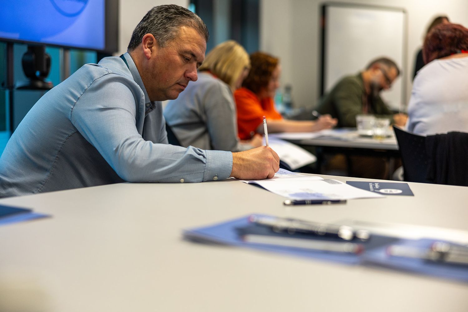 Focused businessman writing notes at a conference table during a professional training workshop.