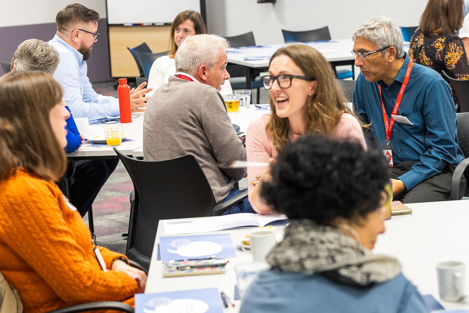 Diverse group of professionals engaged in lively discussion at conference room tables during workshop event.