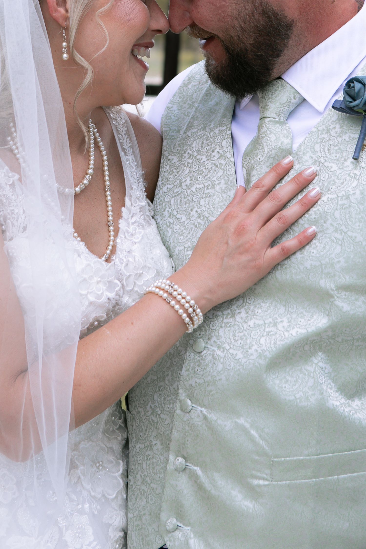 Bride and groom in elegant wedding attire, bride wearing pearl necklace and bracelet, sharing an intimate moment.