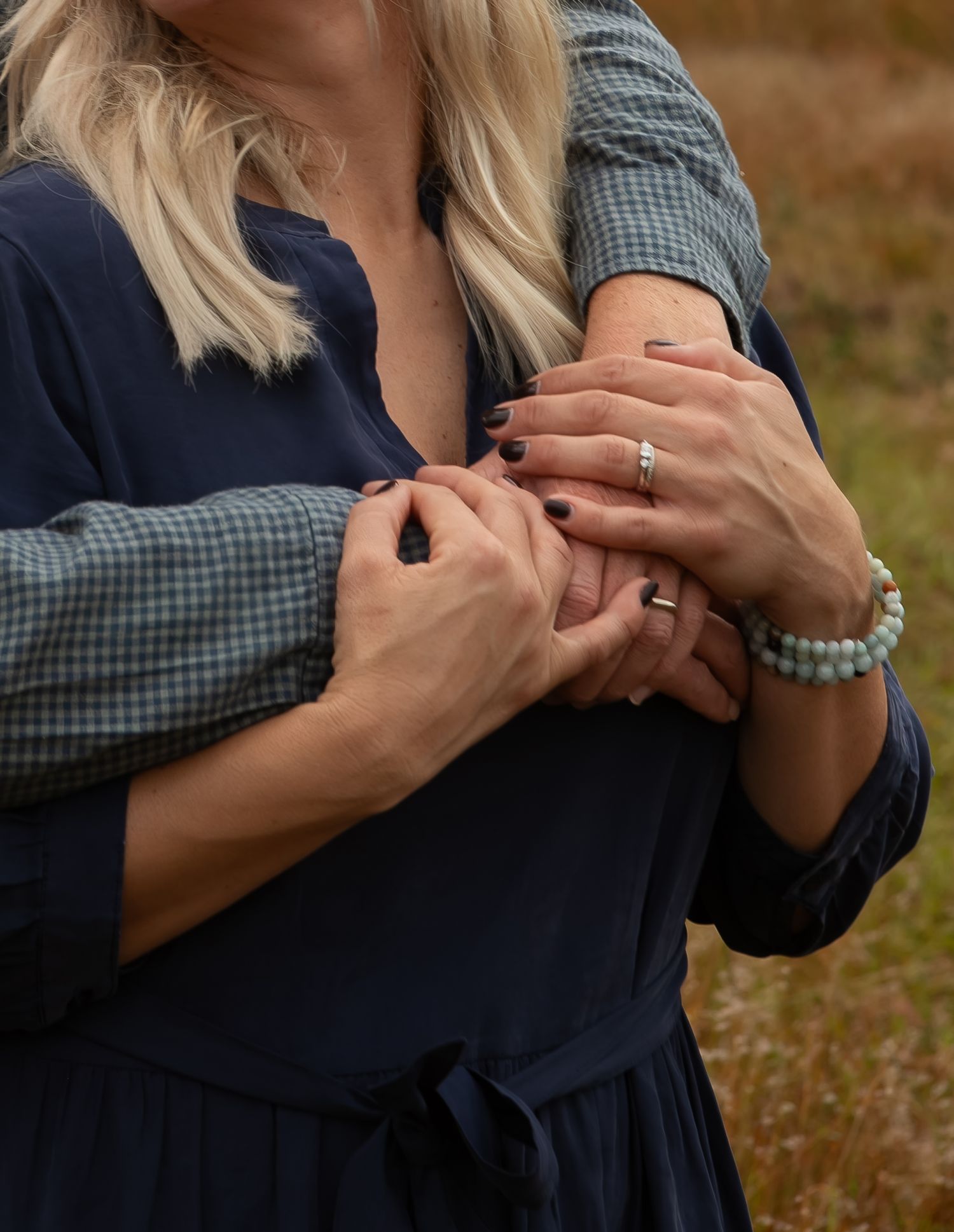 Close-up of couple holding hands, woman wearing a ring and beaded bracelet in navy dress.