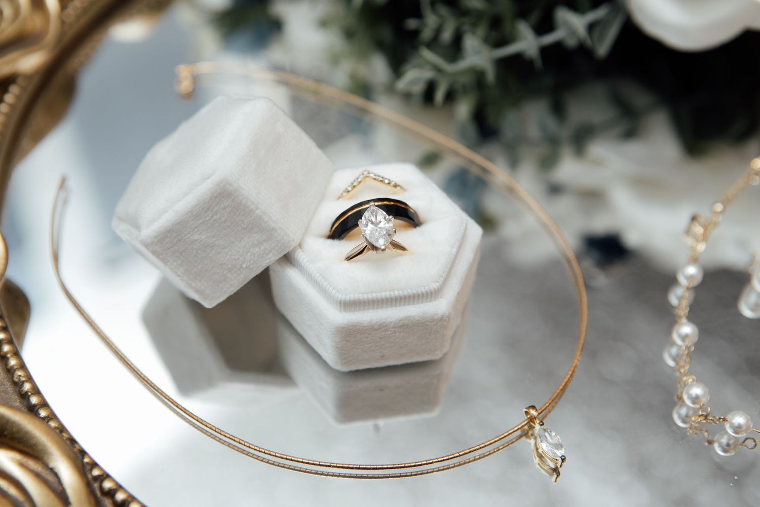 Gold diamond engagement ring and wedding band displayed in a white velvet hexagon ring box on a mirror tray.