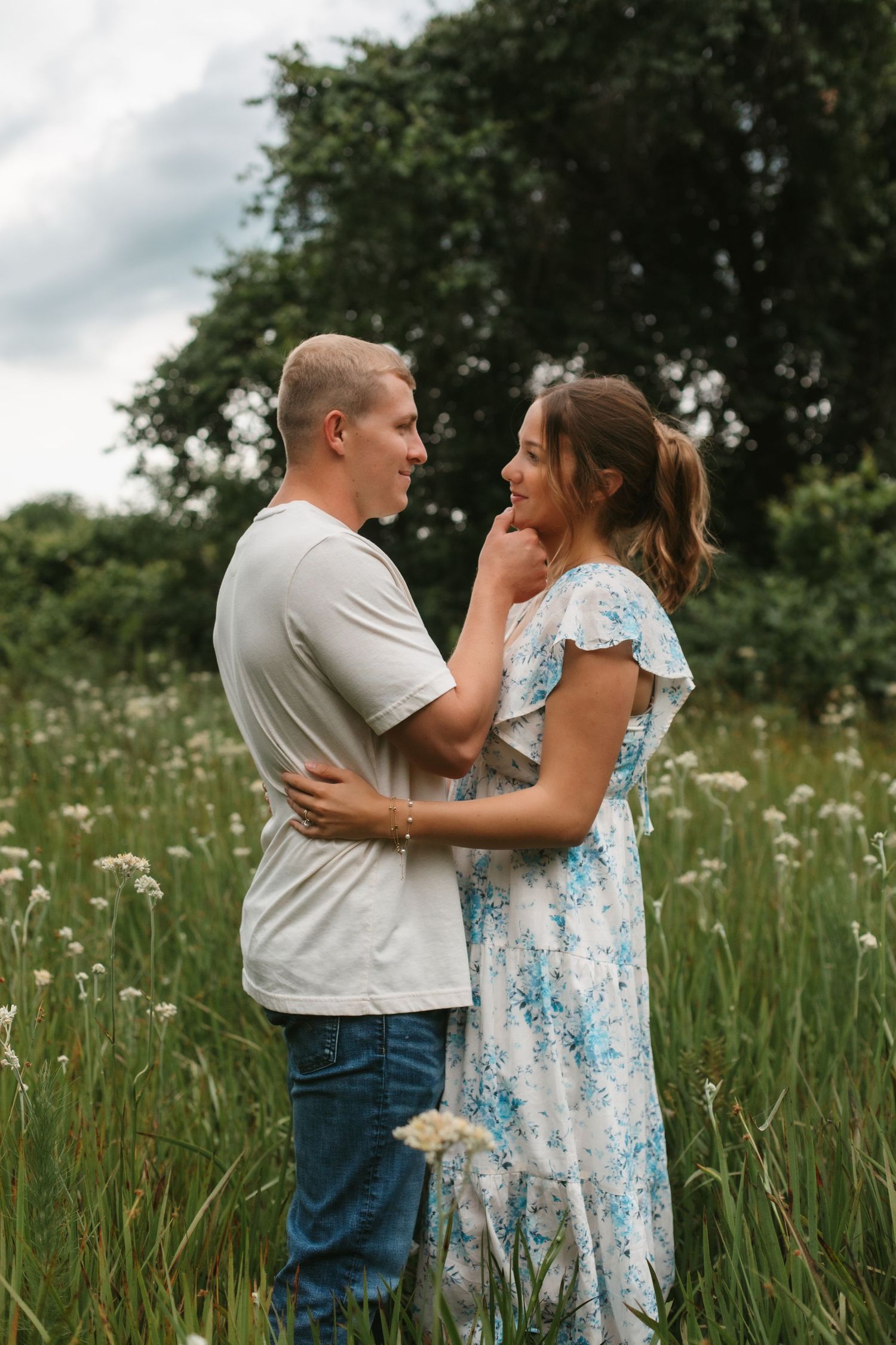 Romantic couple facing each other in a lush green meadow, man gently touching womans chin in a tender moment.