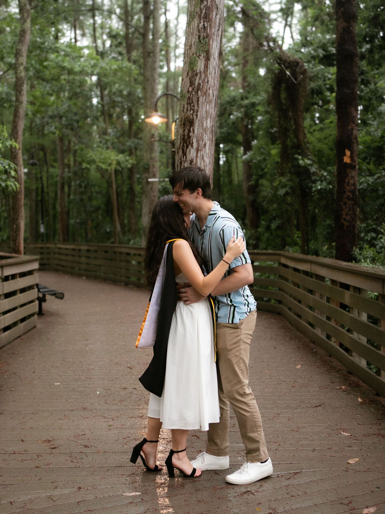 Couple sharing a romantic kiss on a wooden bridge in a lush green forest setting.