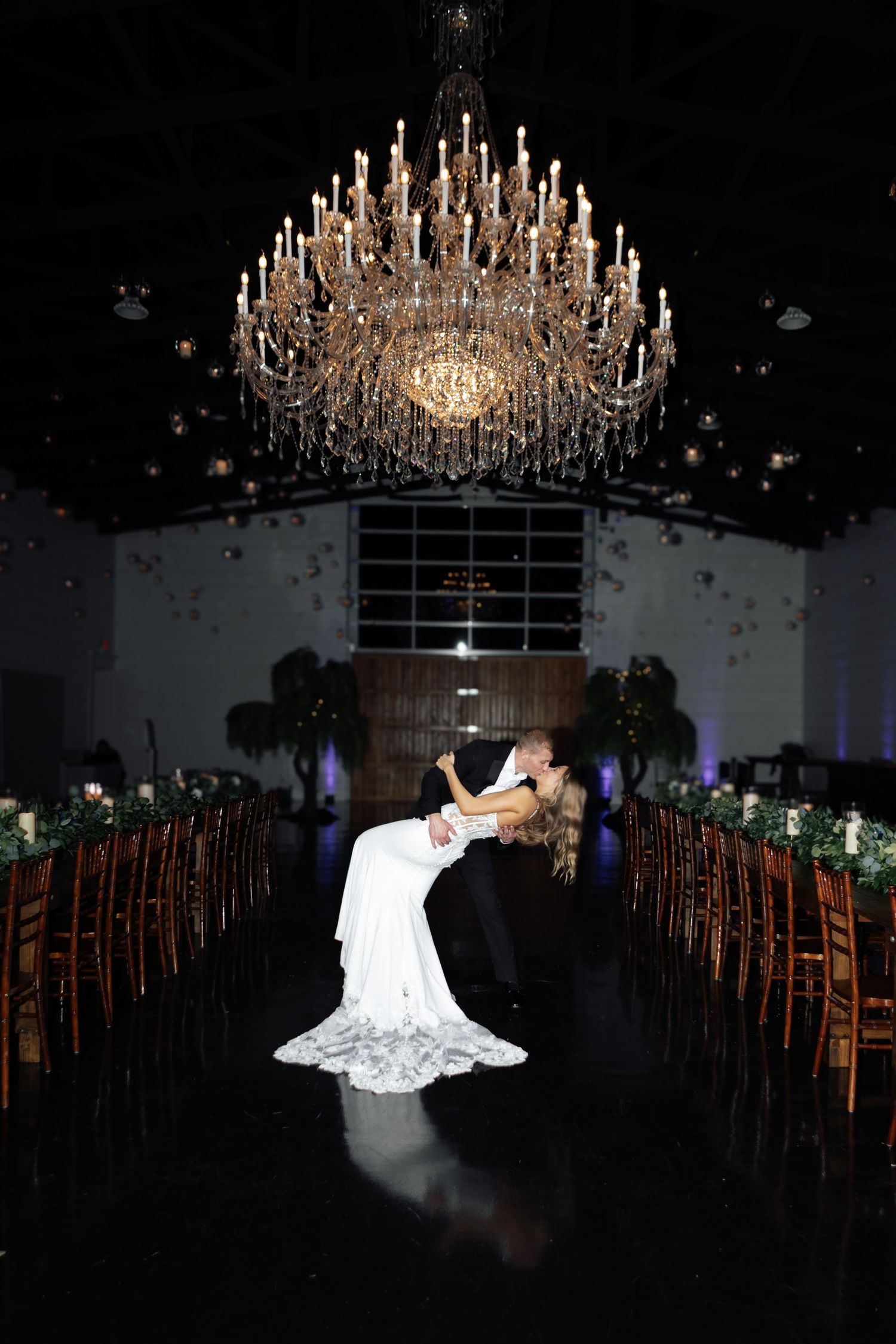 Bride and groom share romantic dip under grand chandelier in elegant wedding venue.