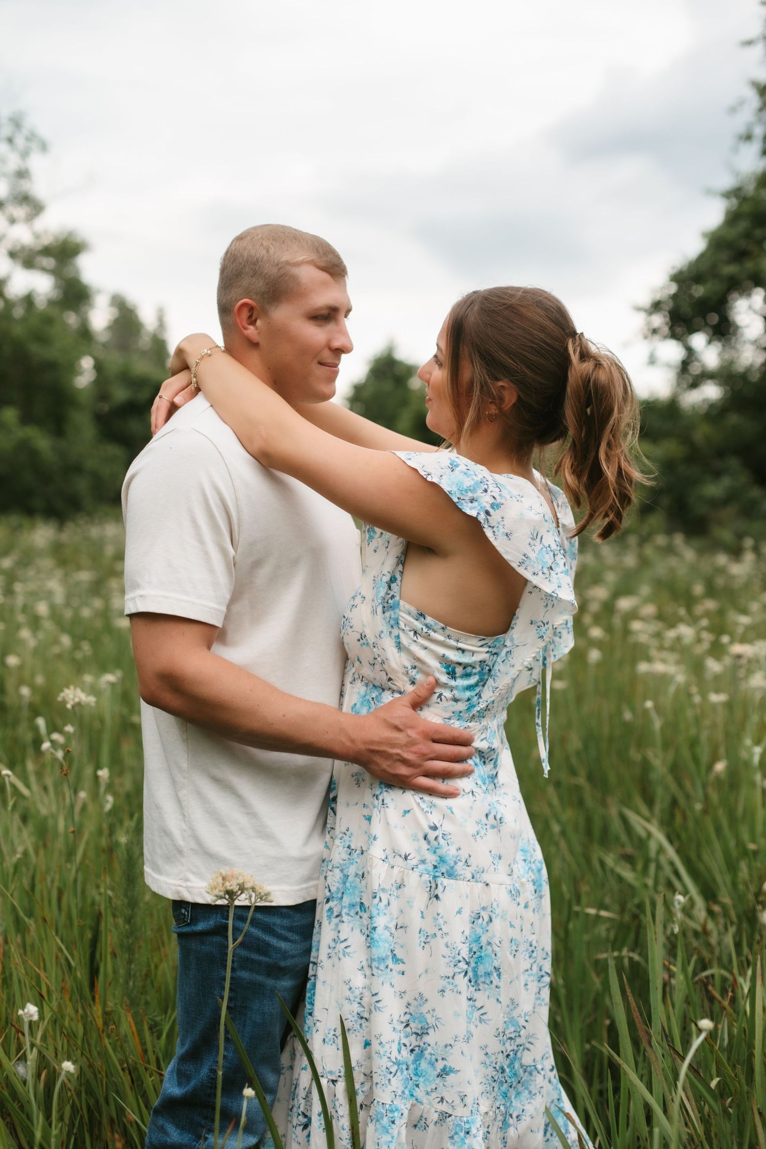 Couple embracing in a wildflower field, woman in floral dress with arms around mans neck, romantic outdoor portrait.