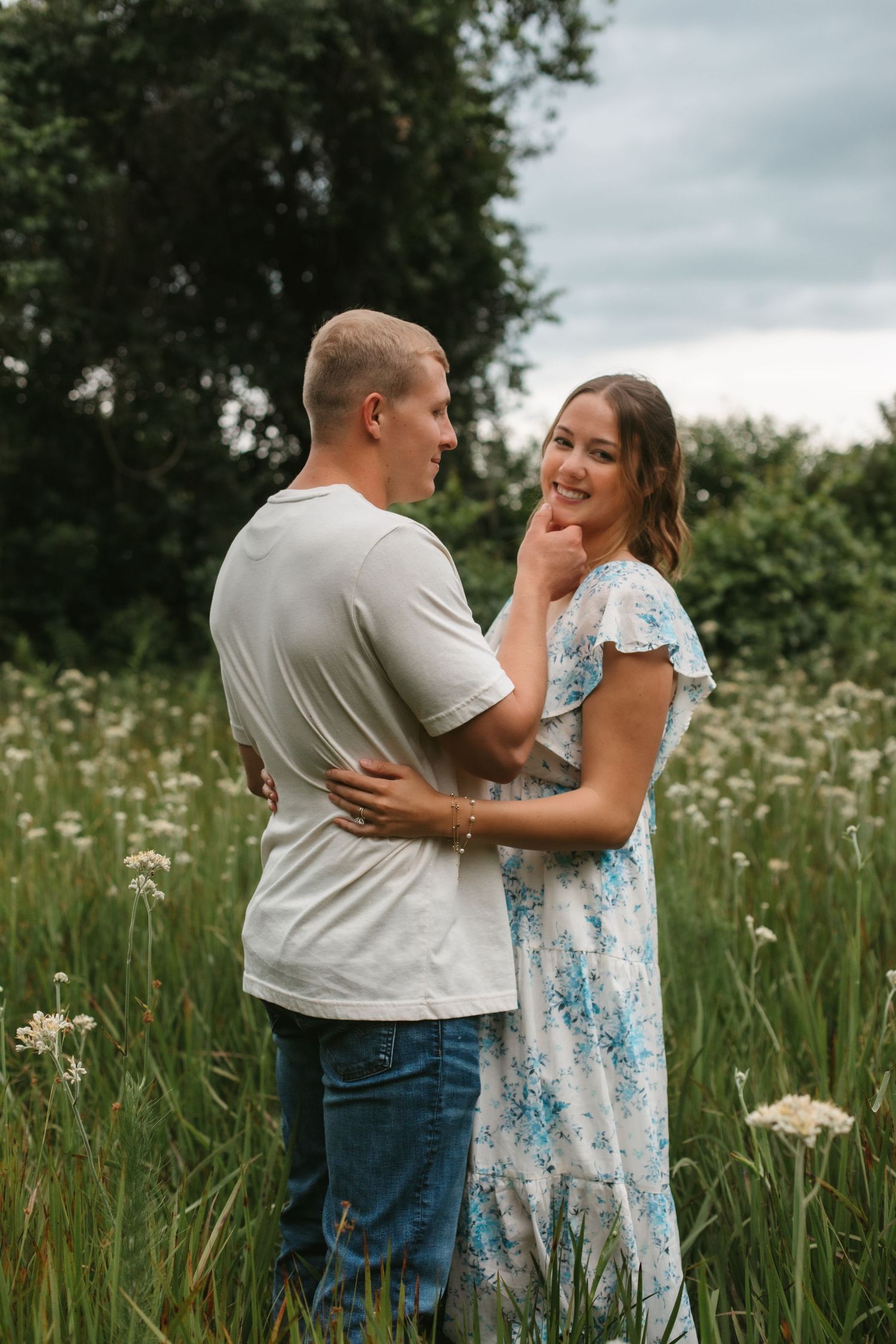 Couple embracing in a wildflower field, woman in floral dress smiling at camera while man holds her close.