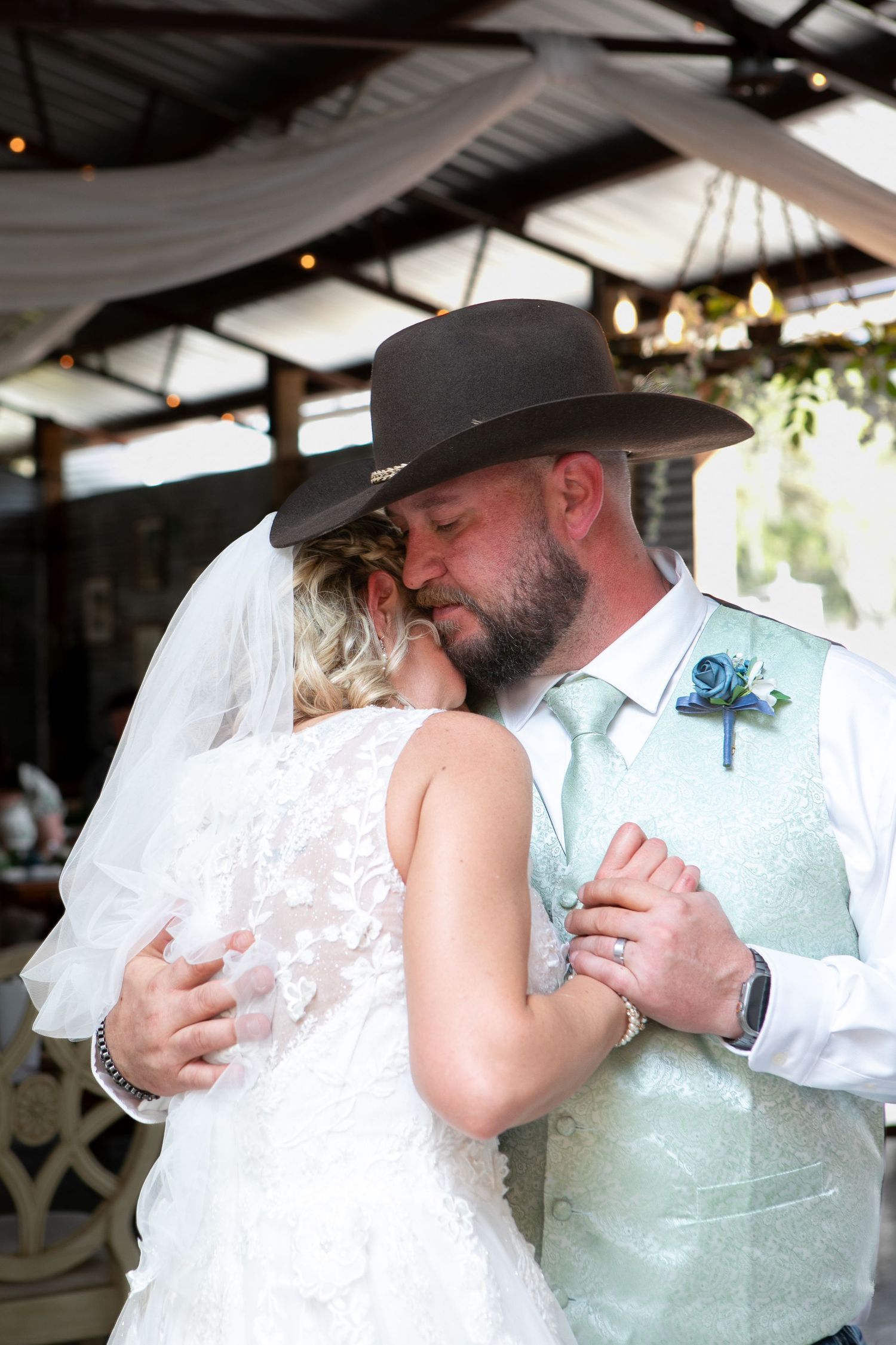 Bride and groom share intimate first dance, groom wearing brown cowboy hat and mint vest with blue boutonniere.