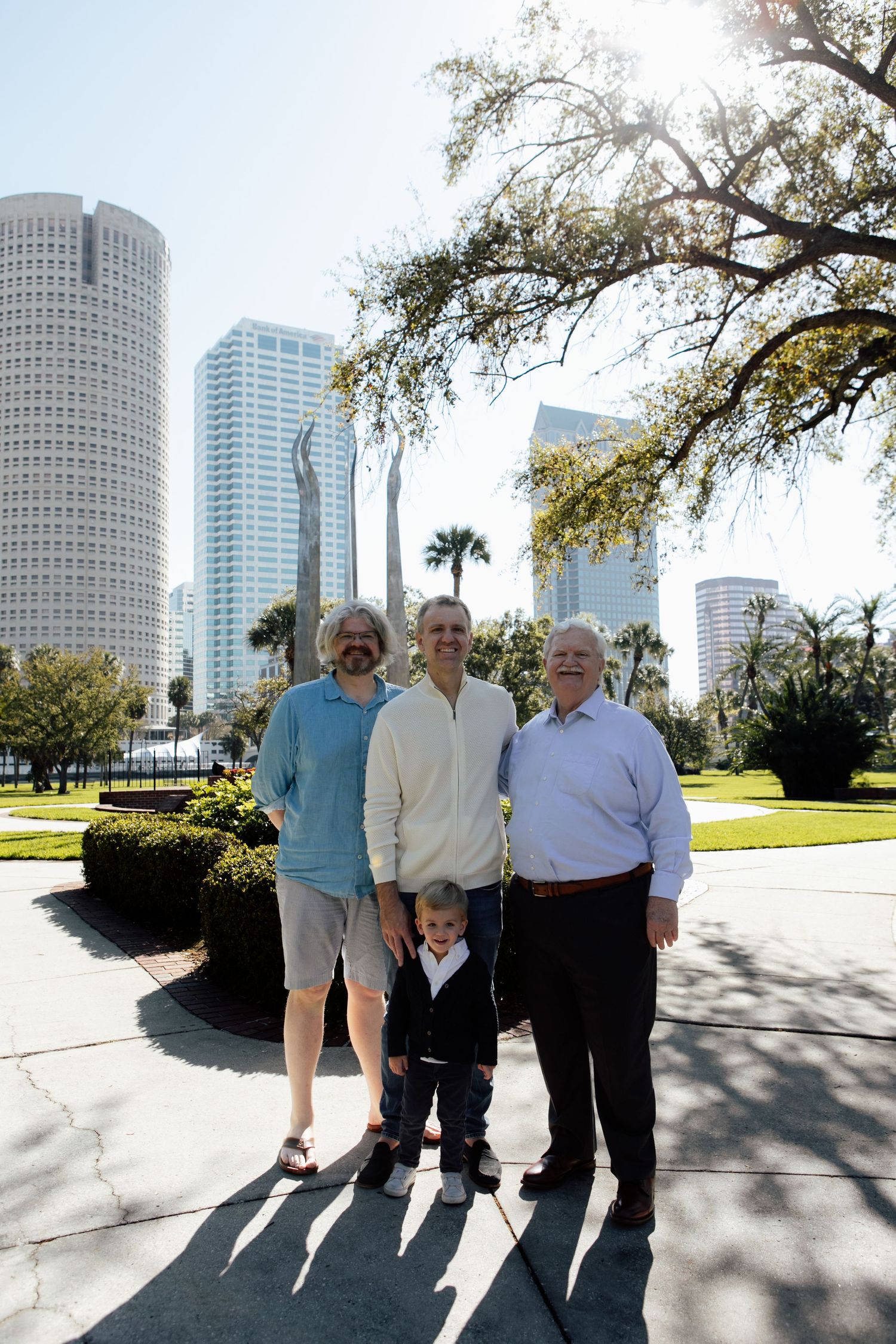 Three generations of men pose with young boy in front of Tampa city skyline on sunny day.