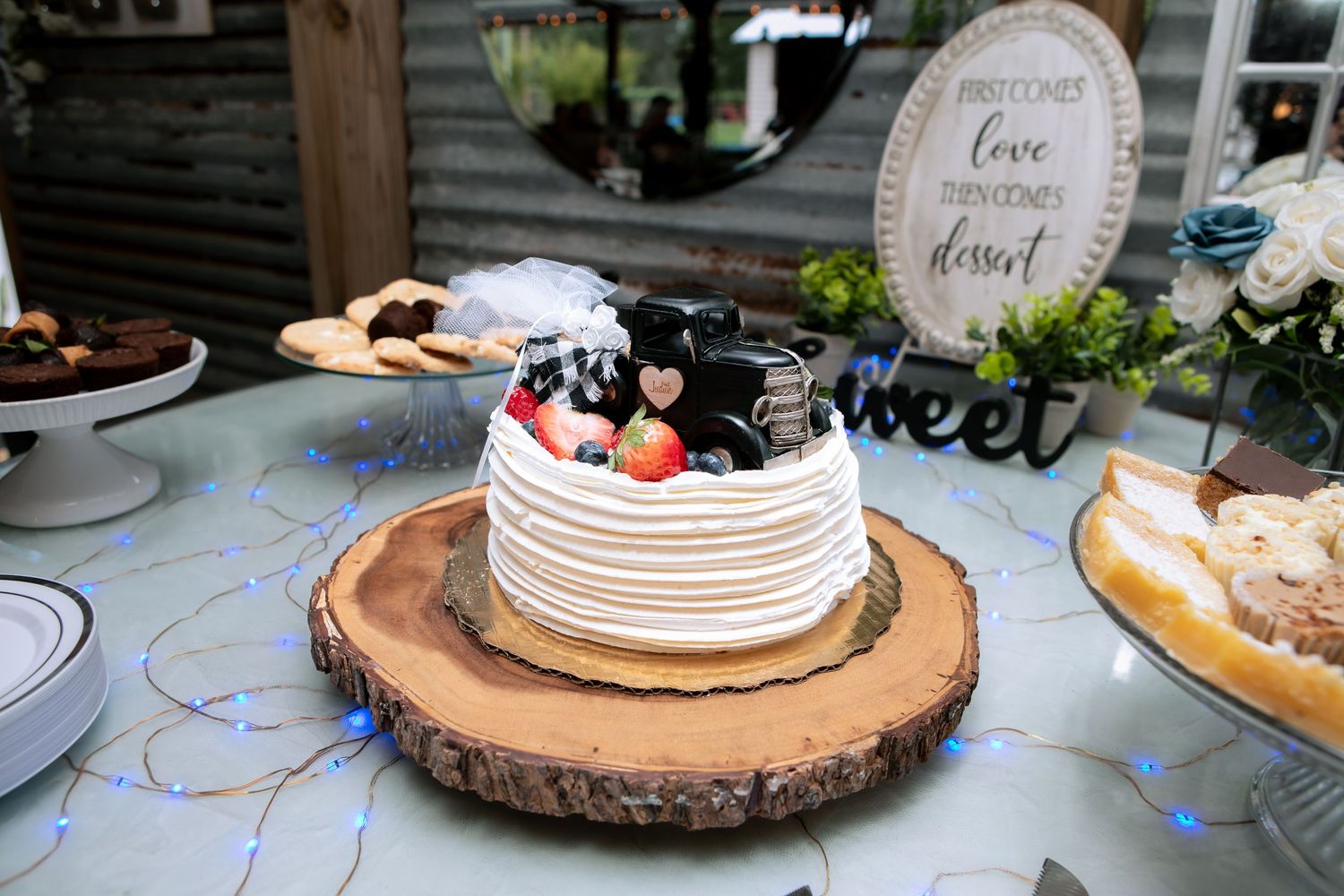 Elegant white layered wedding cake topped with fresh berries on a rustic wood slice at a dessert table.