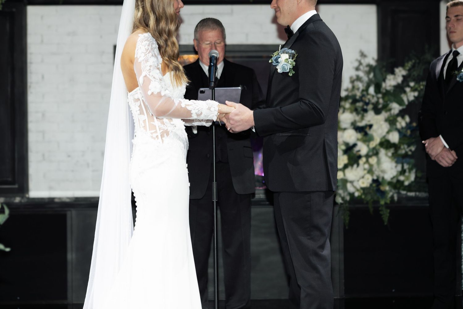 Bride and groom exchanging vows at wedding altar with officiant and white floral arrangements.