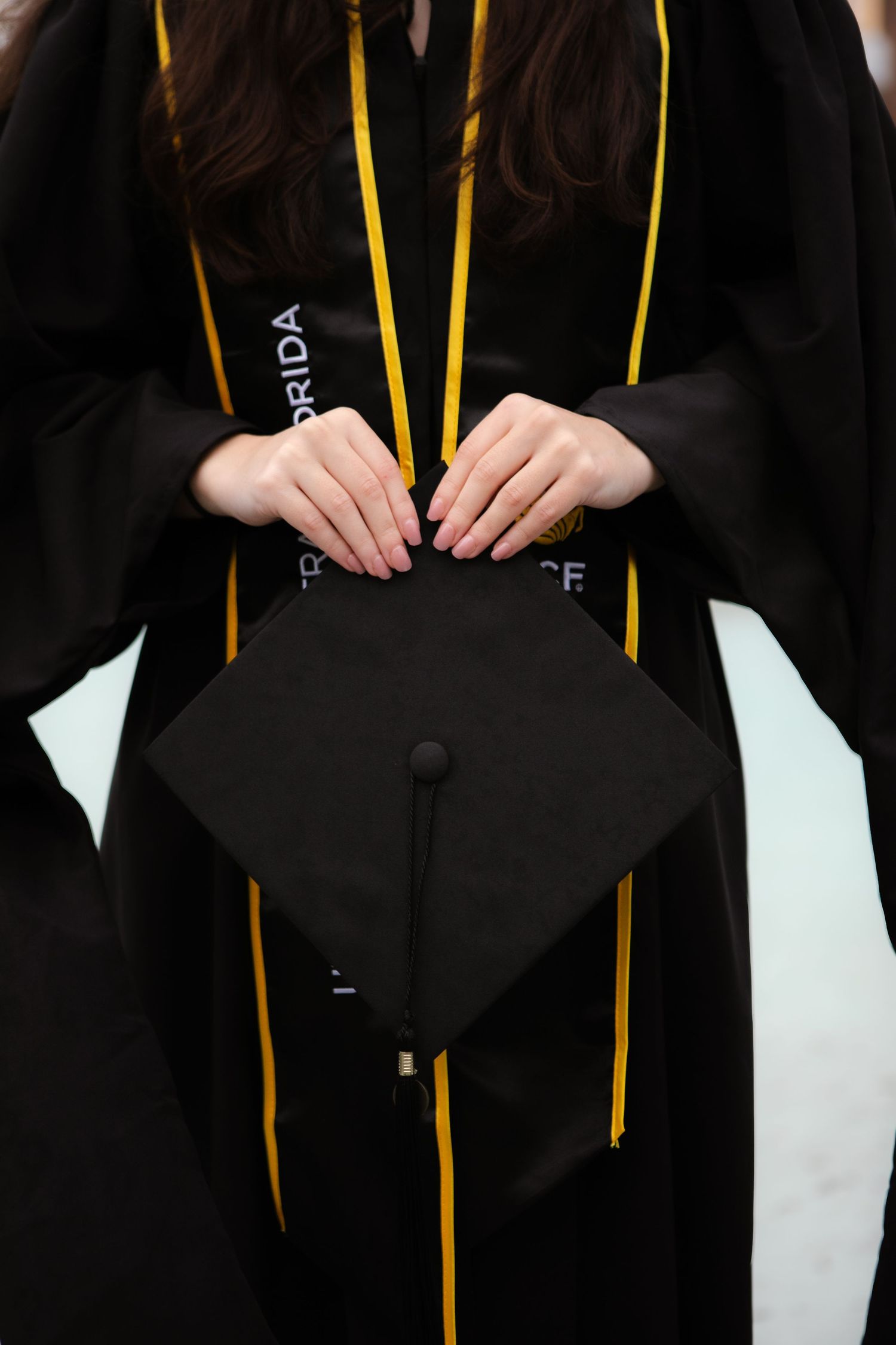 Graduate in black gown holds mortarboard cap with gold stole at University of Florida commencement ceremony.