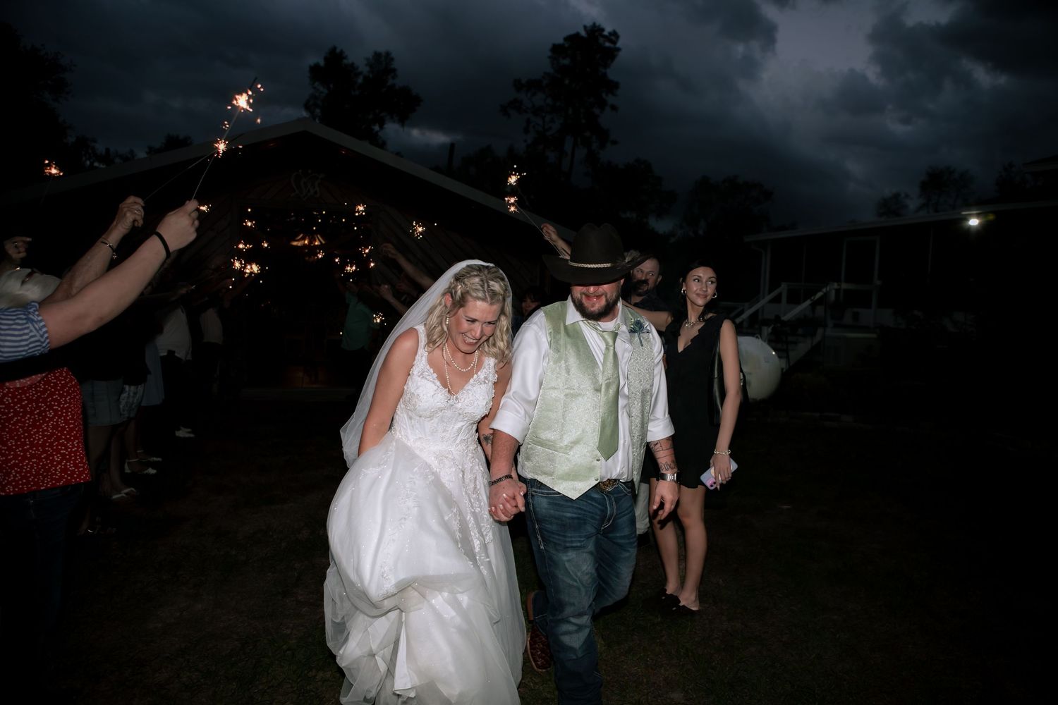 Bride and groom exit through sparkler send-off at night during rustic outdoor wedding reception celebration.