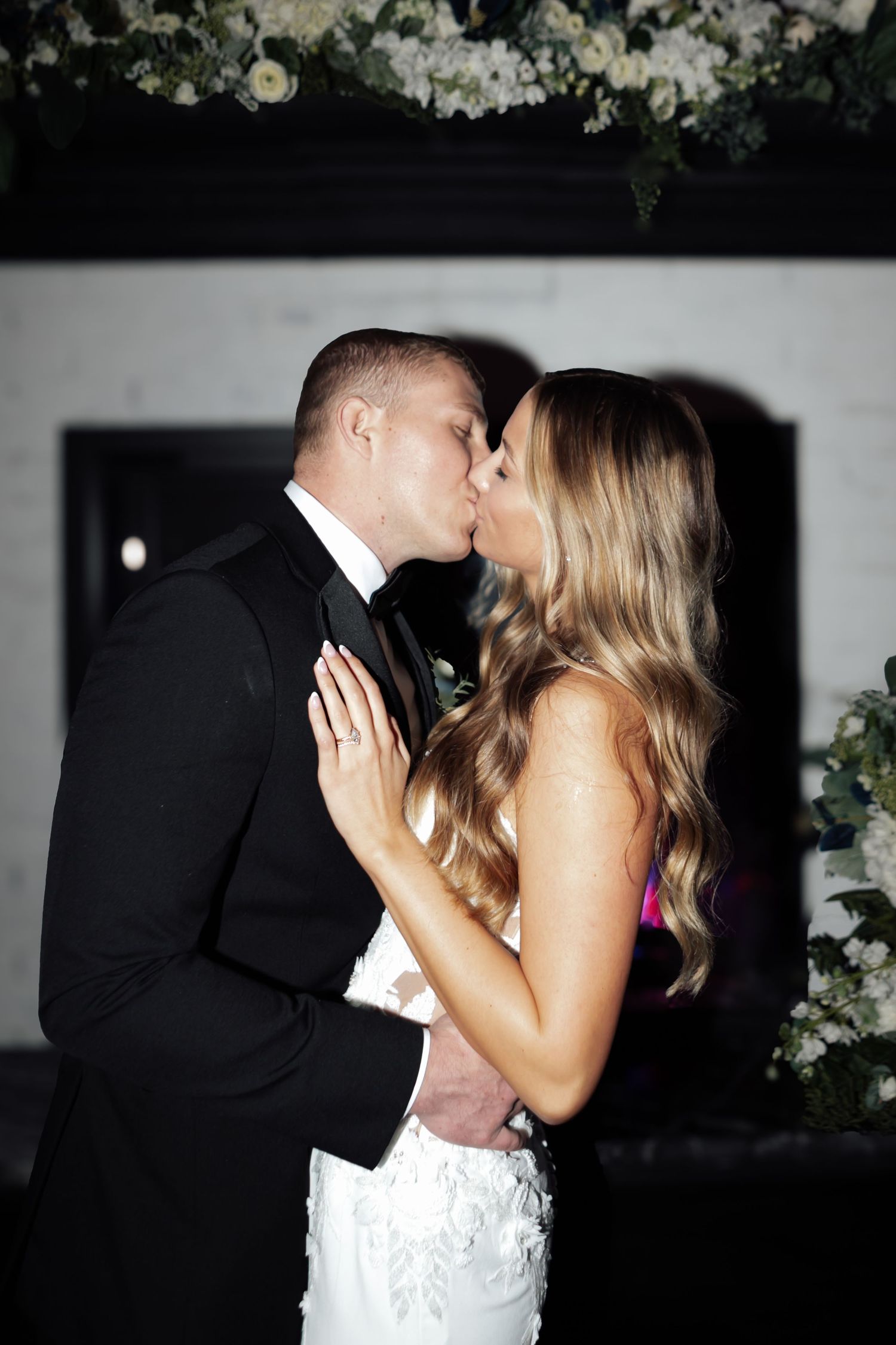 Bride and groom share their first kiss at wedding ceremony with floral arch backdrop.