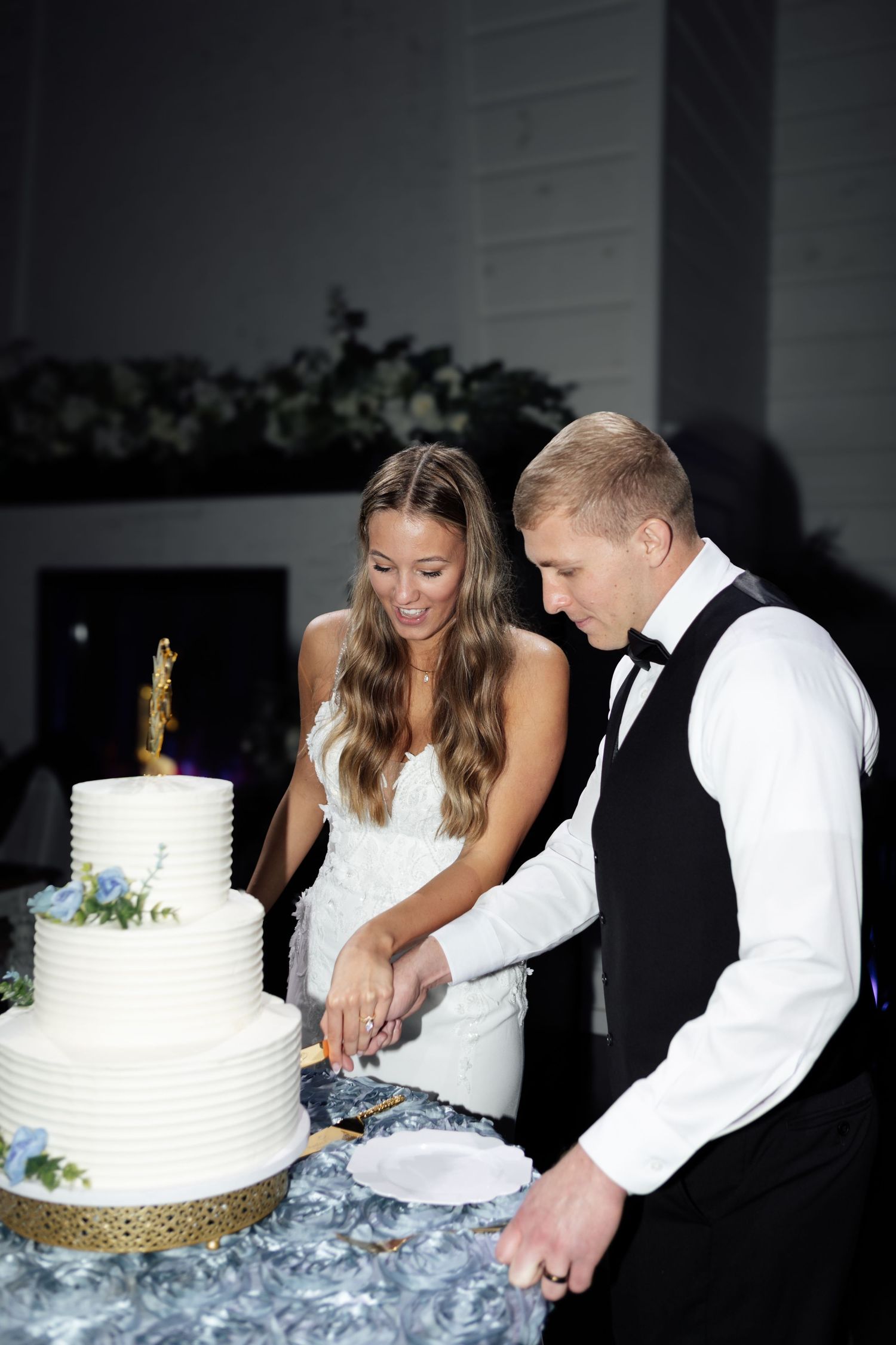 Bride and groom cutting a three-tier white wedding cake with gold base together.