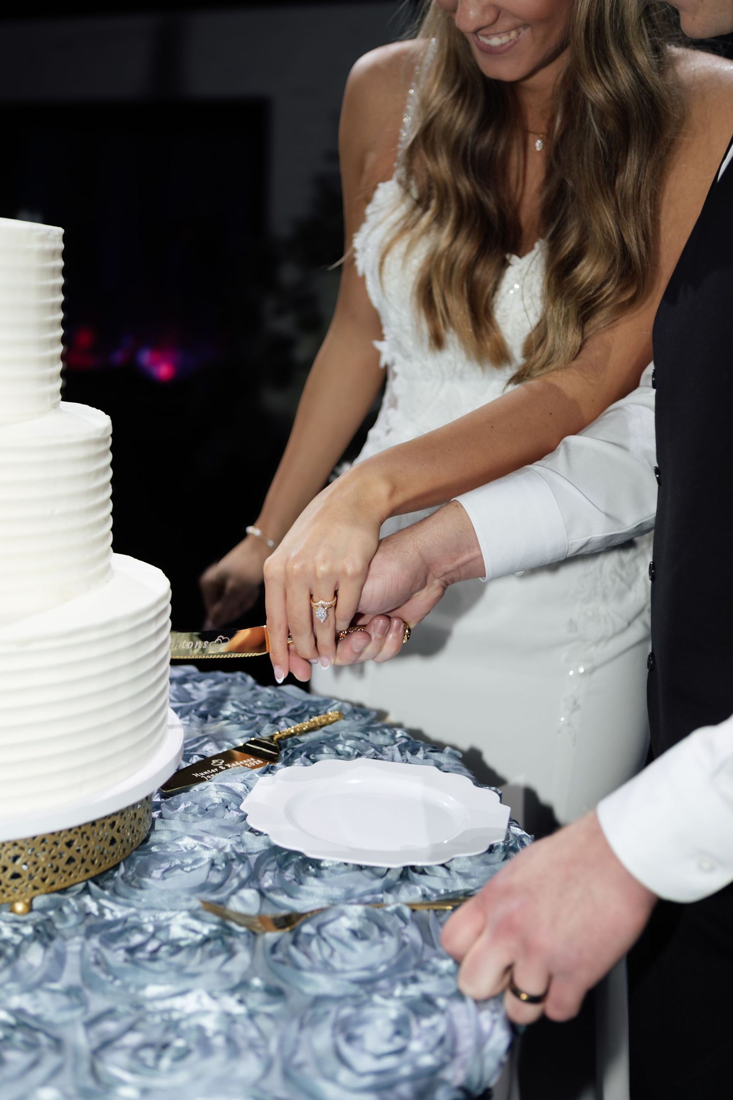 Smiling bride and groom cut three-tier white wedding cake at reception together.