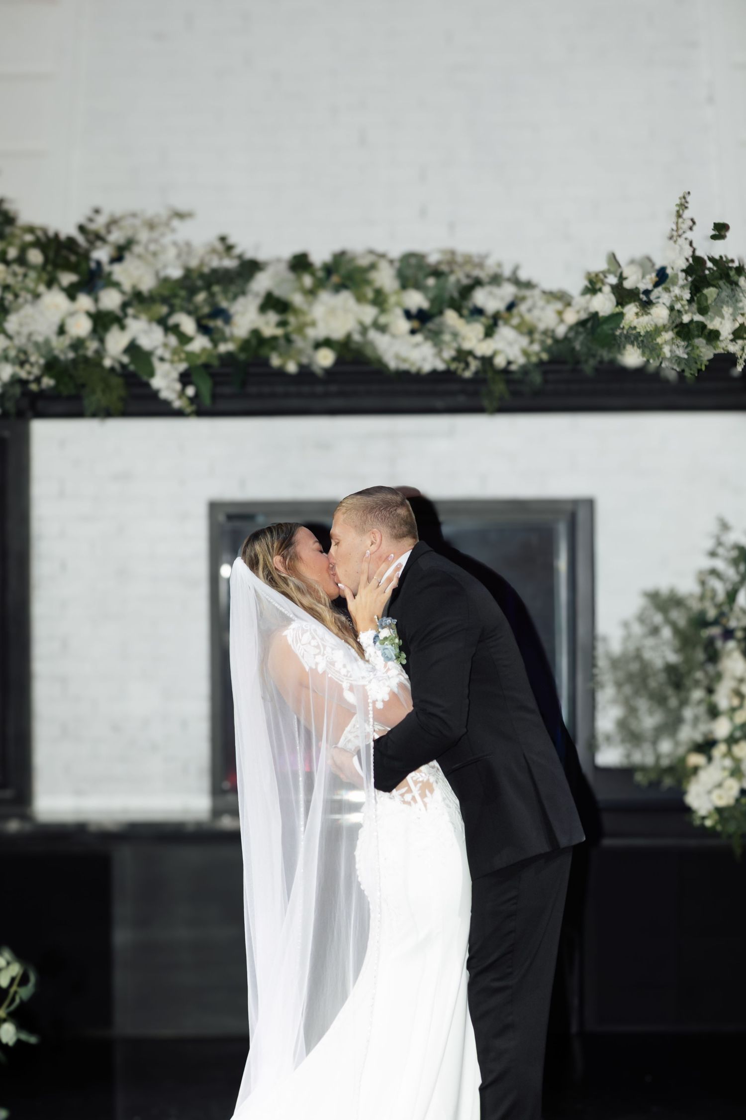 Bride and groom sharing their first kiss at the altar decorated with white floral arrangements.