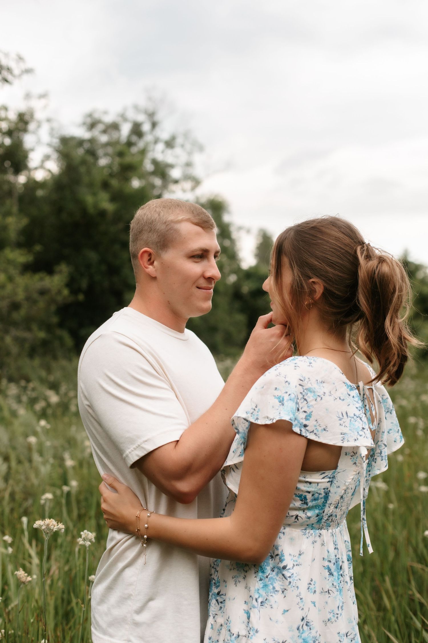 A couple embraces in a wildflower field, the man gently touching the woman's face as they share a tender moment.