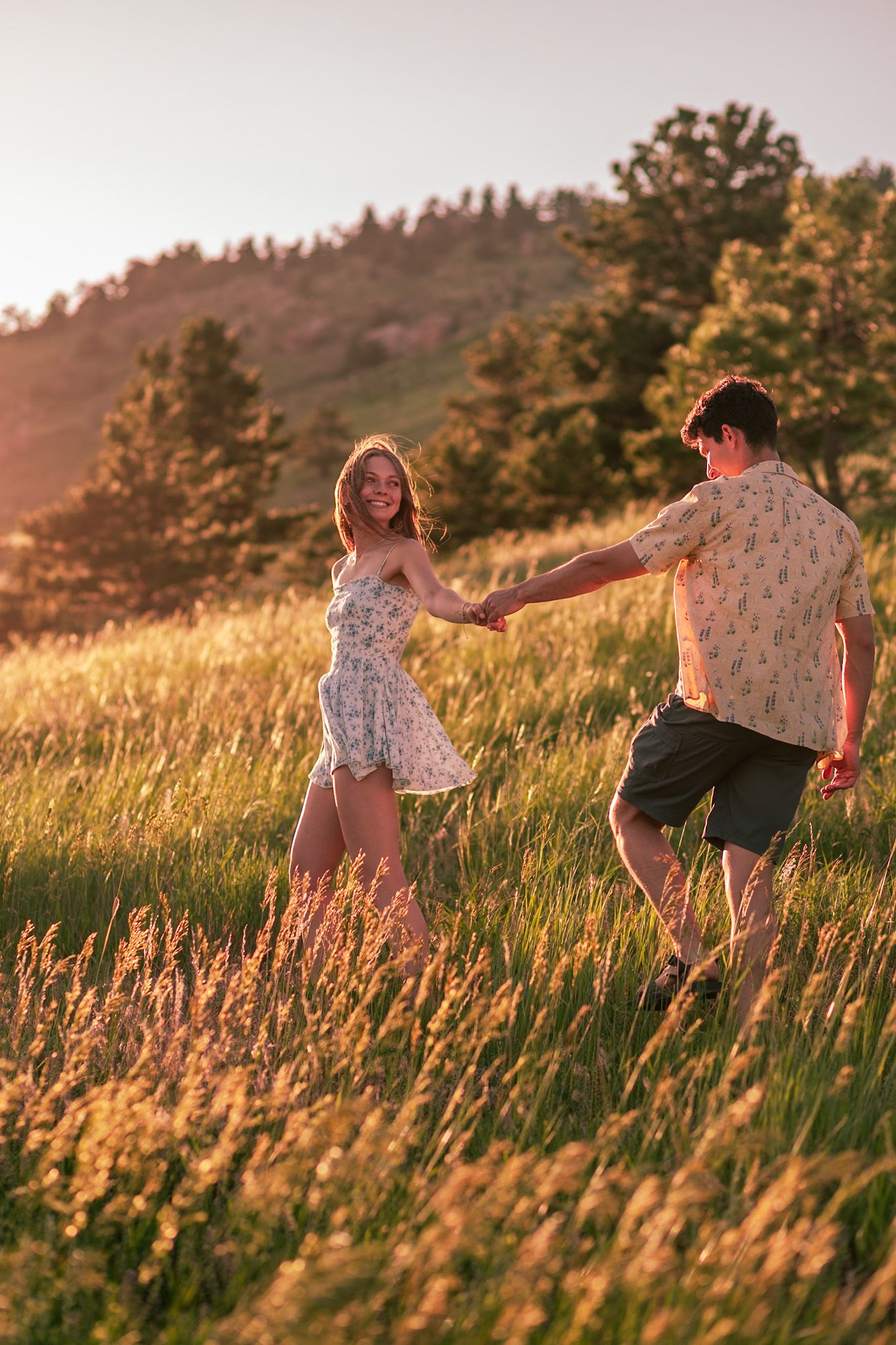 Couple running in a field with the mountainous backdrop of Horsetooth Falls in Fort Collins, Colorado.