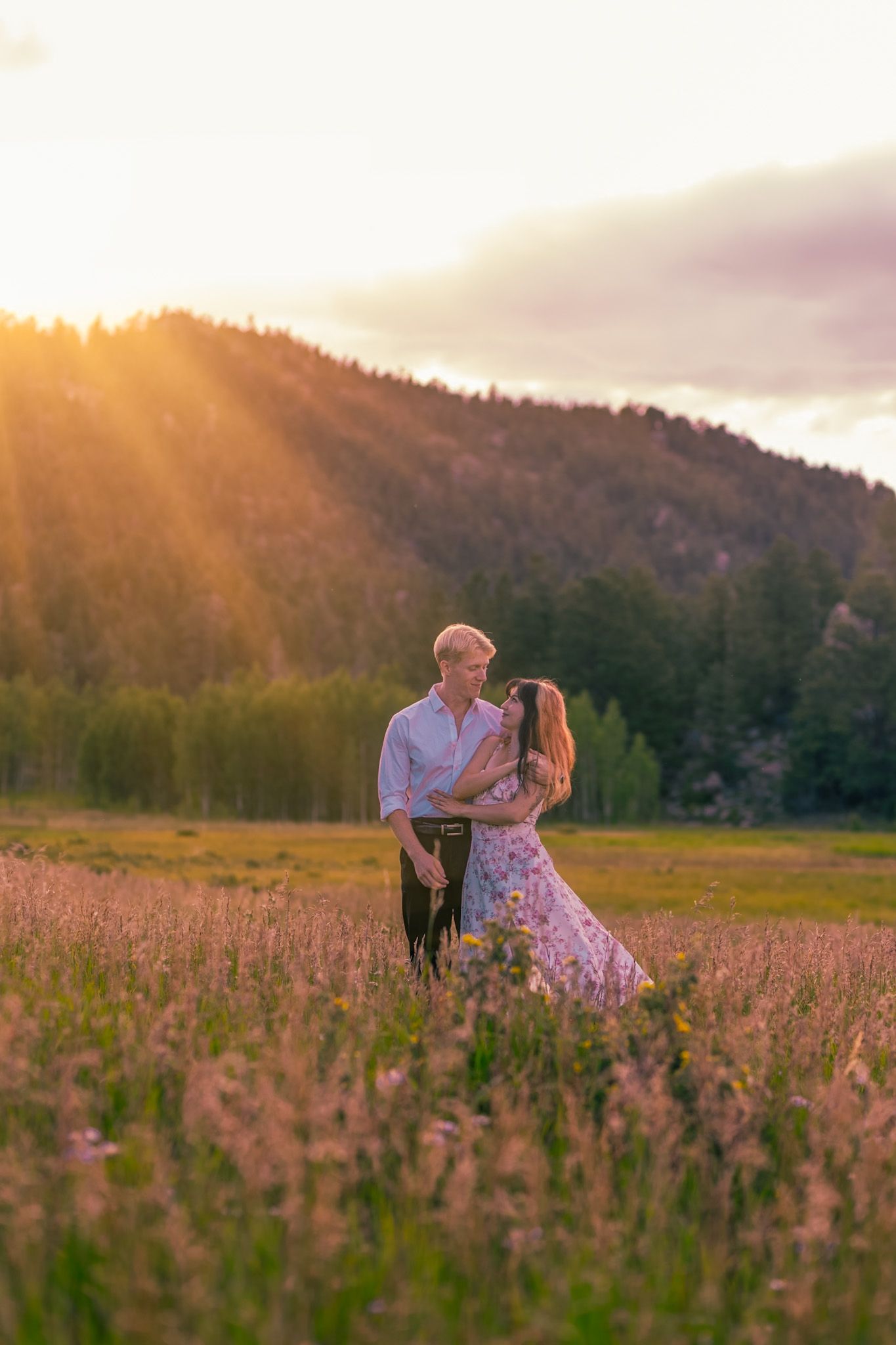 Couple embracing in flowery meadow with mountainous sunset backdrop in Rocky Mountain National Park, Colorado.
