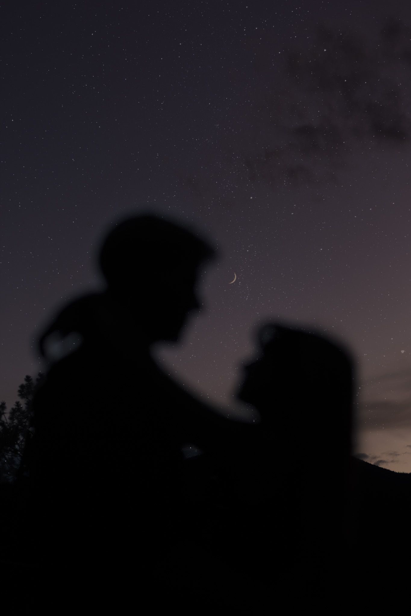 Silhouettes against starry night sky with crescent moon in Rocky Mountain National Park, Colorado.