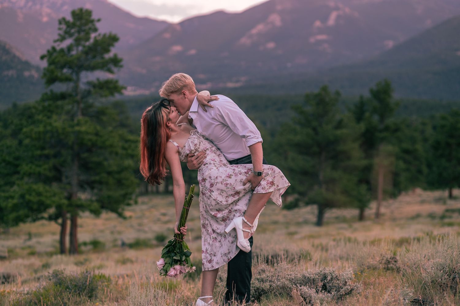 Couple shares intimate romantic moment in mountain field during sunset in Rocky Mountain National Park, Colorado.